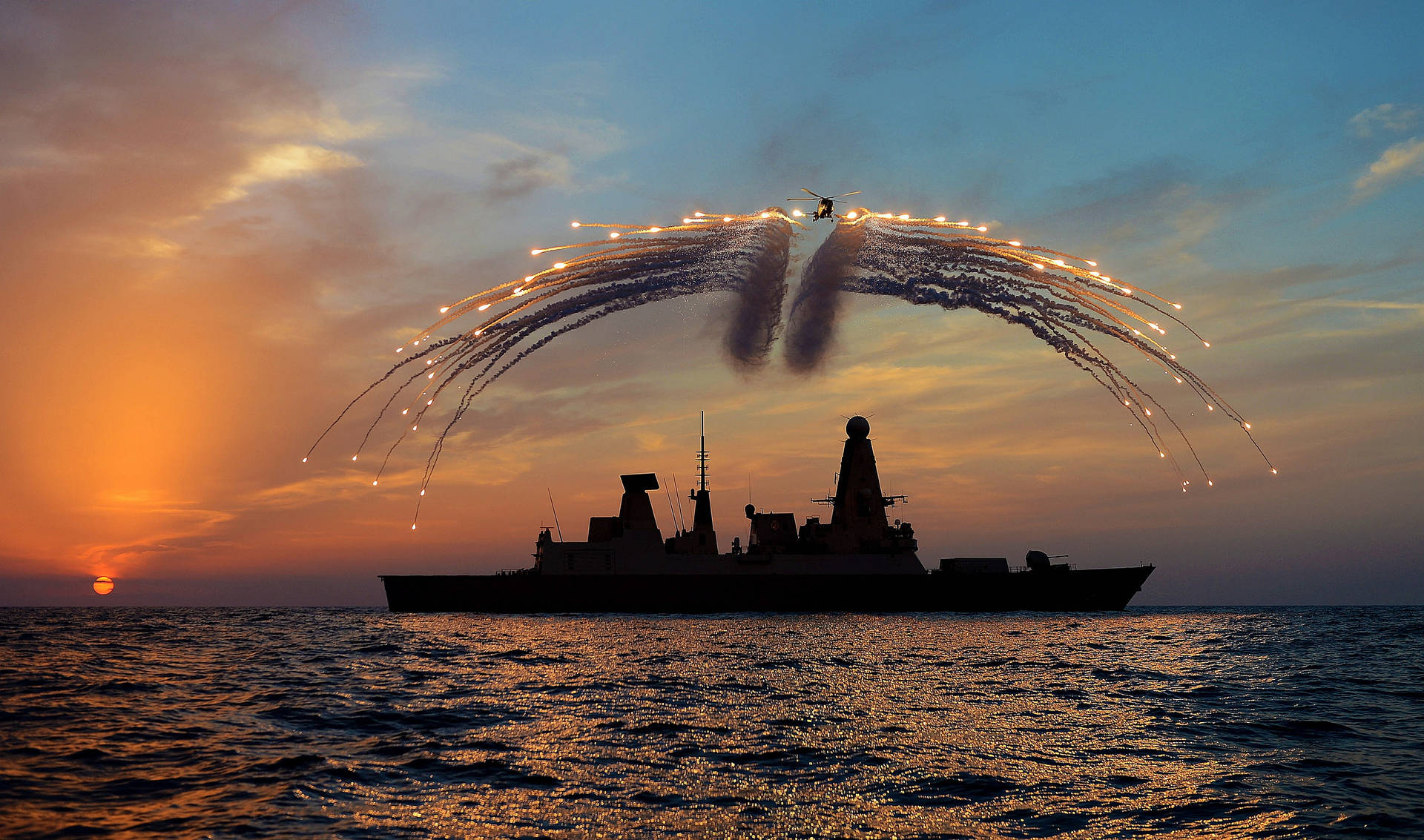 夕陽下的軍艦與直升機在海洋上空釋放照明彈