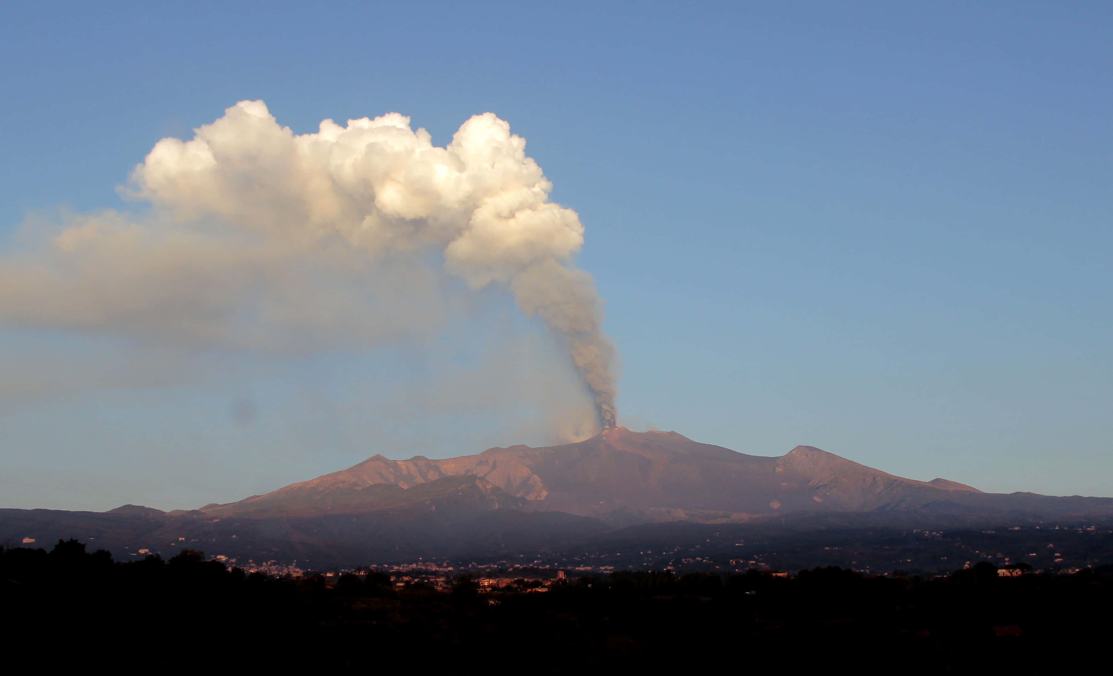 西西里島埃特納火山日出全景 壁紙 — 火山爆發，向遠方城鎮上空晴朗的藍天噴出大量火山灰和煙霧。