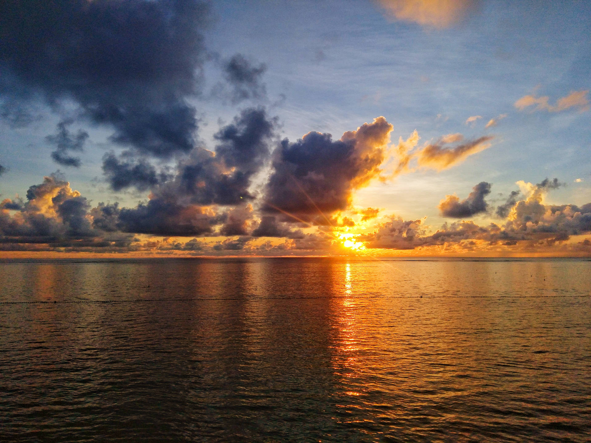 夕陽映照海洋，彩色雲朵和金色水面倒影