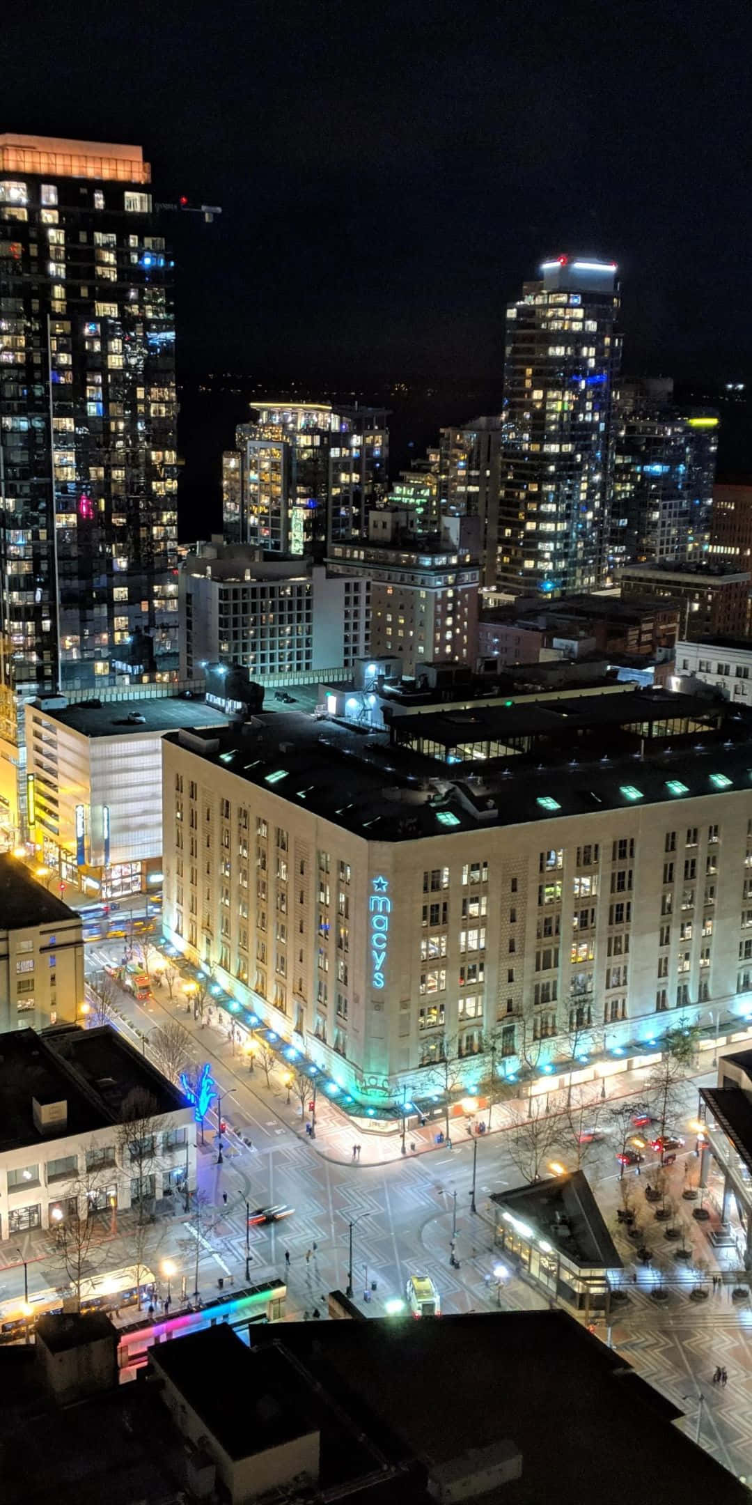 西雅圖夏日晴空下的 Pixel 3 壁紙 — 從高空俯瞰繁華城市景觀的夜景，燈火通明的摩天大樓和閃耀的Macy's建築位於繁忙的十字路口。