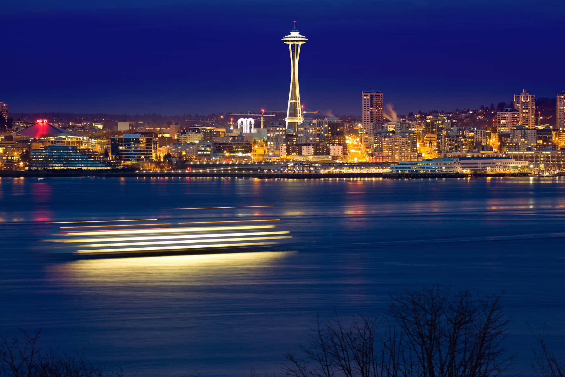 西雅圖城市夜景，太空針塔和水面上的船隻燈光軌跡。