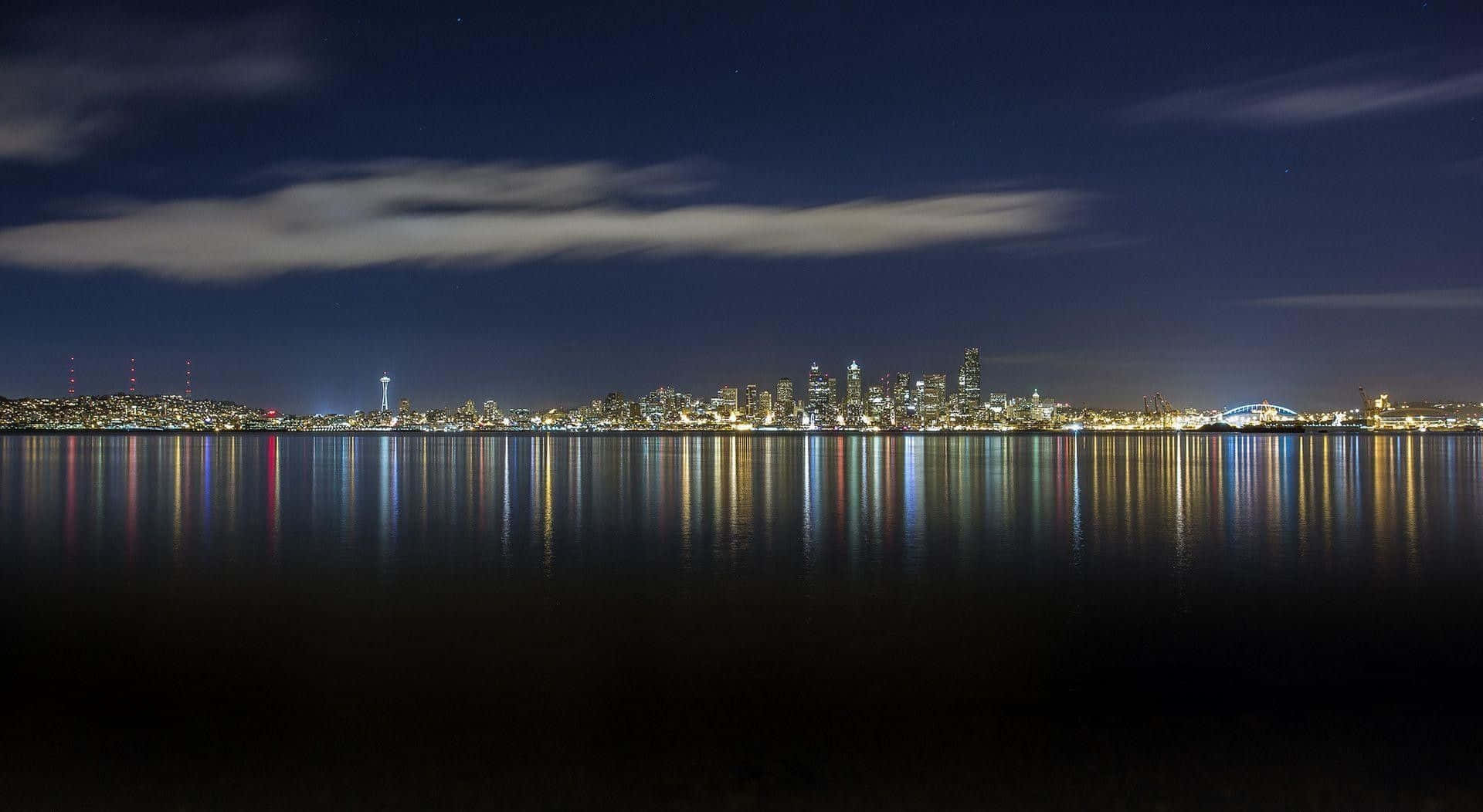 西雅圖夜景天際線，城市燈光在繁星天空下倒映在水中。