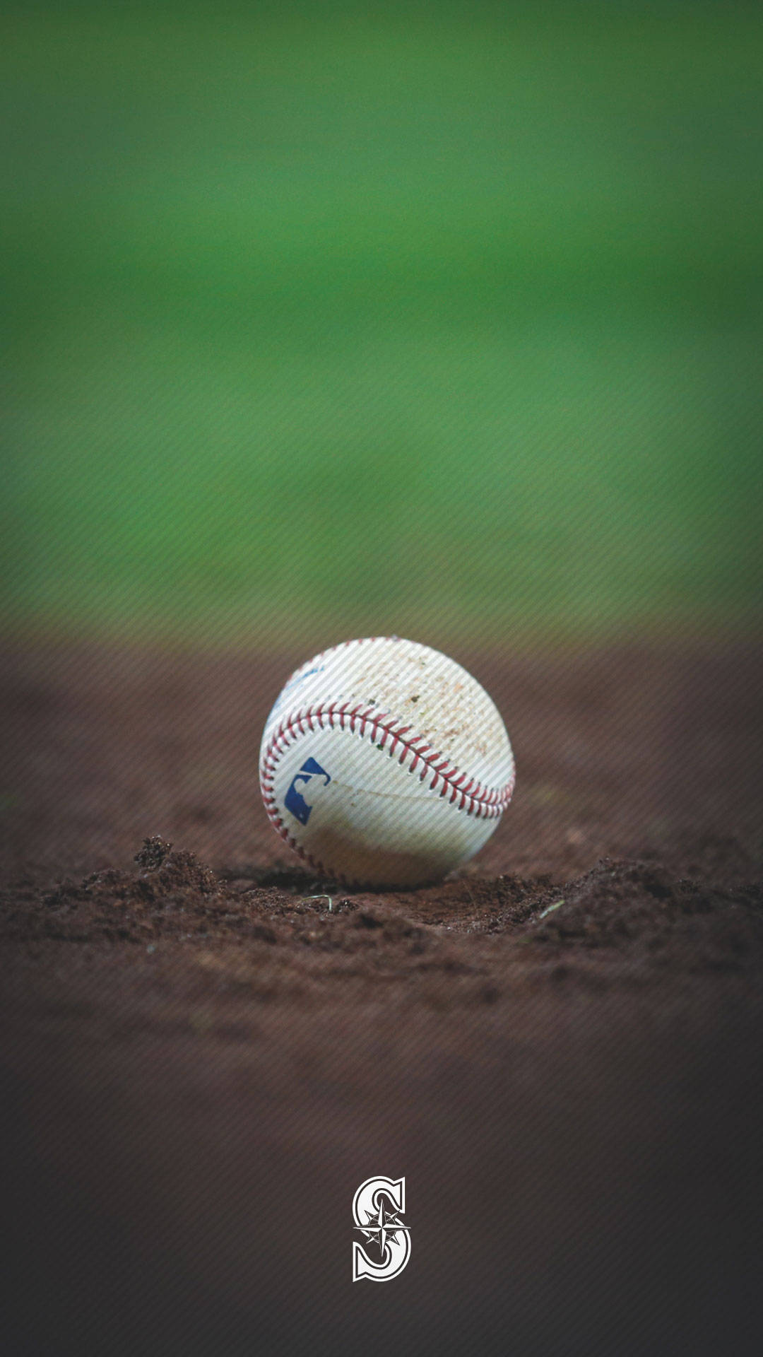 西雅圖水手隊棒球落地特寫 壁紙 — 一個磨損的棒球放在裂開的棕色泥土上，背景是模糊的綠色球場。