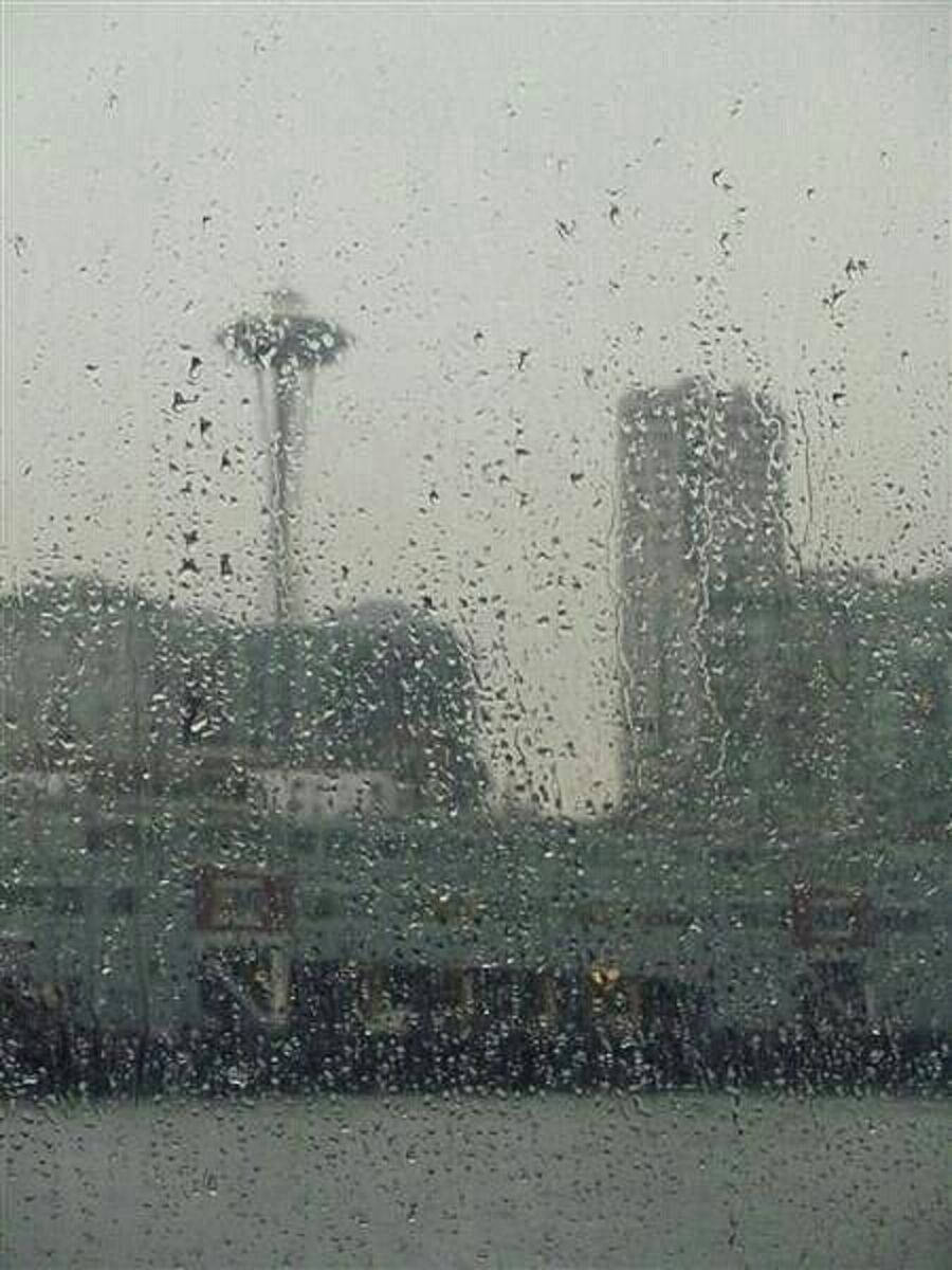 窗戶上的雨滴，透過薄霧可見西雅圖太空針塔和城市景觀。