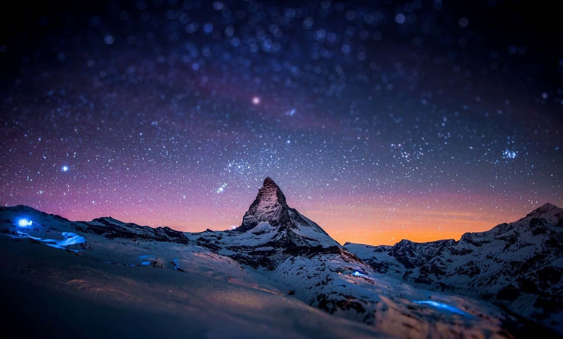 覆雪山峰下的繁星夜空 壁紙 — 白雪覆蓋的馬特洪峰在星空暮色下聳立，帶有紫橙色漸變，雪坡上閃爍著藍色光芒。