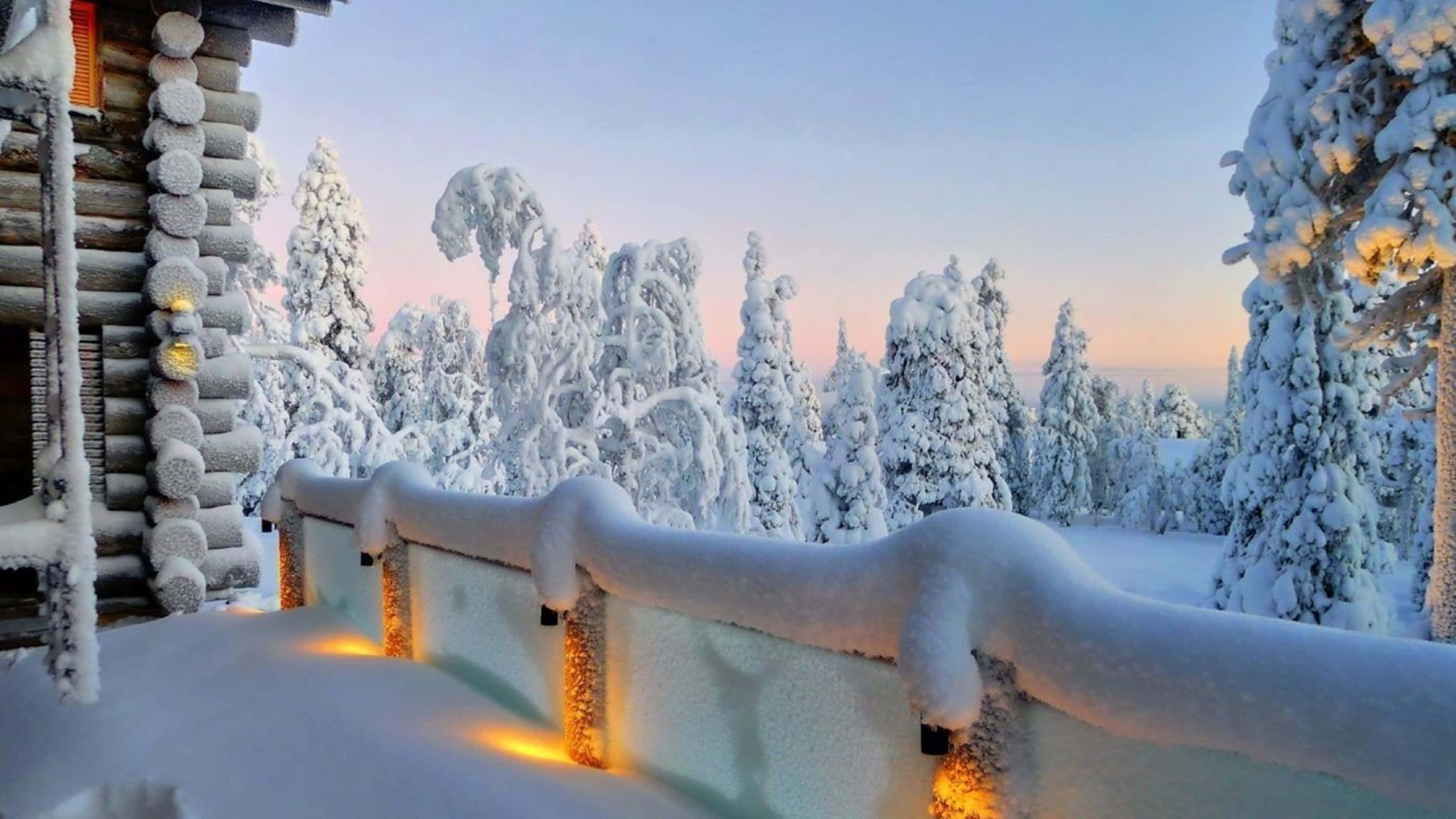 覆雪木屋門廊 4K 壁紙 — 白雪覆蓋的木屋門廊在黃昏時分，在寧靜的冬季森林背景下，用串燈溫暖地發光。