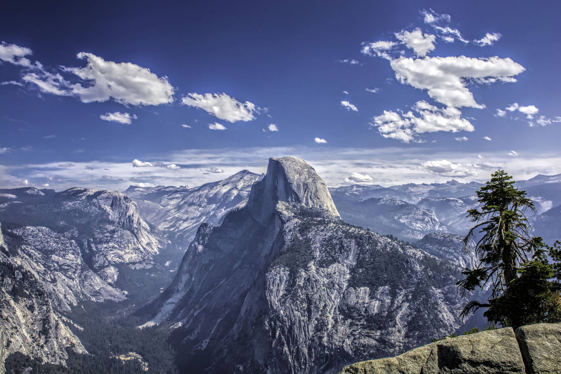 Half Dome 山峰在明亮的藍天和零星雲朵下。
