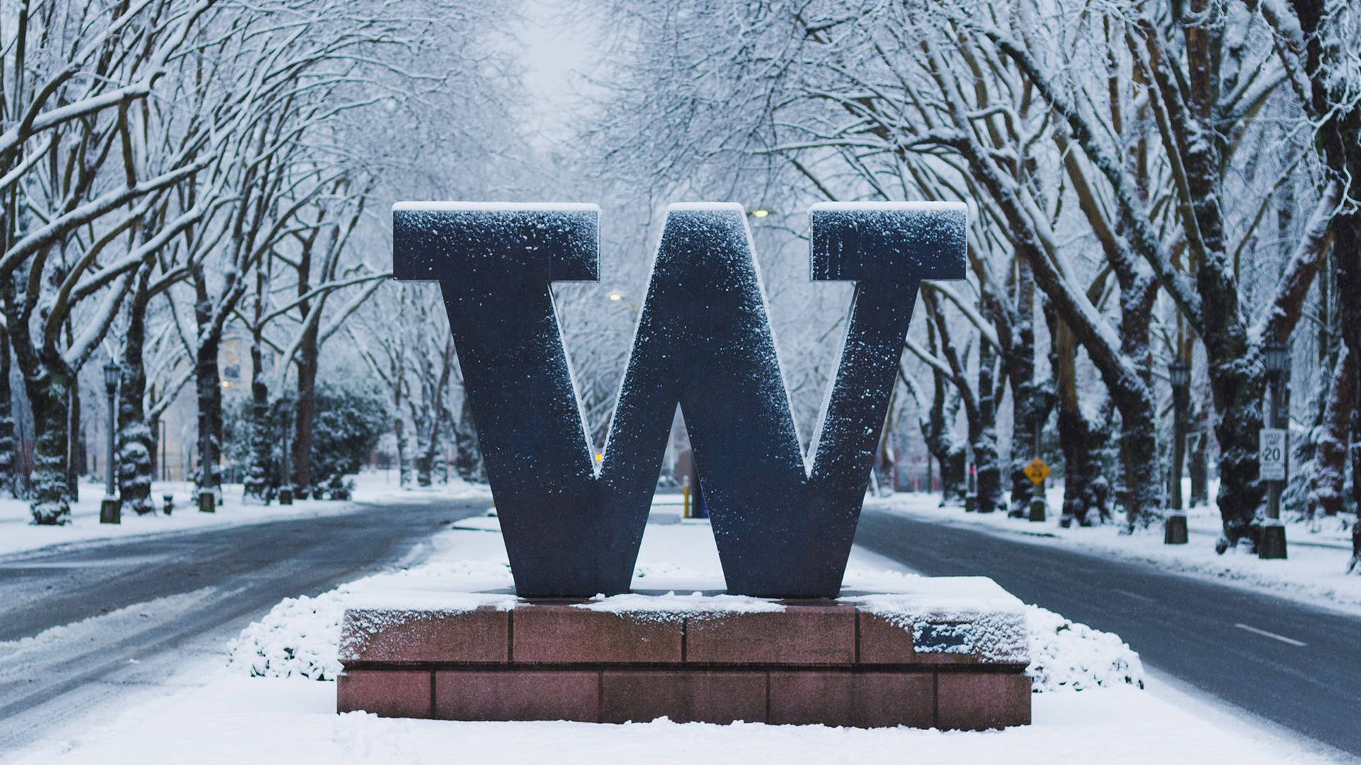 冬季街景中，磚砌基座上一個被雪覆蓋的大型字母W。