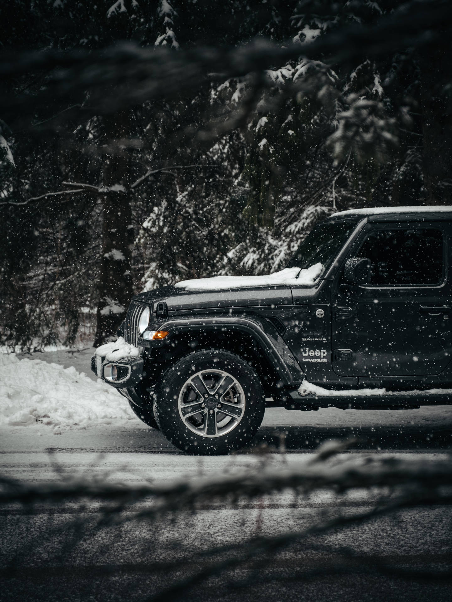 黑色Jeep Wrangler停泊在冬季森林雪路上，降雪中。
