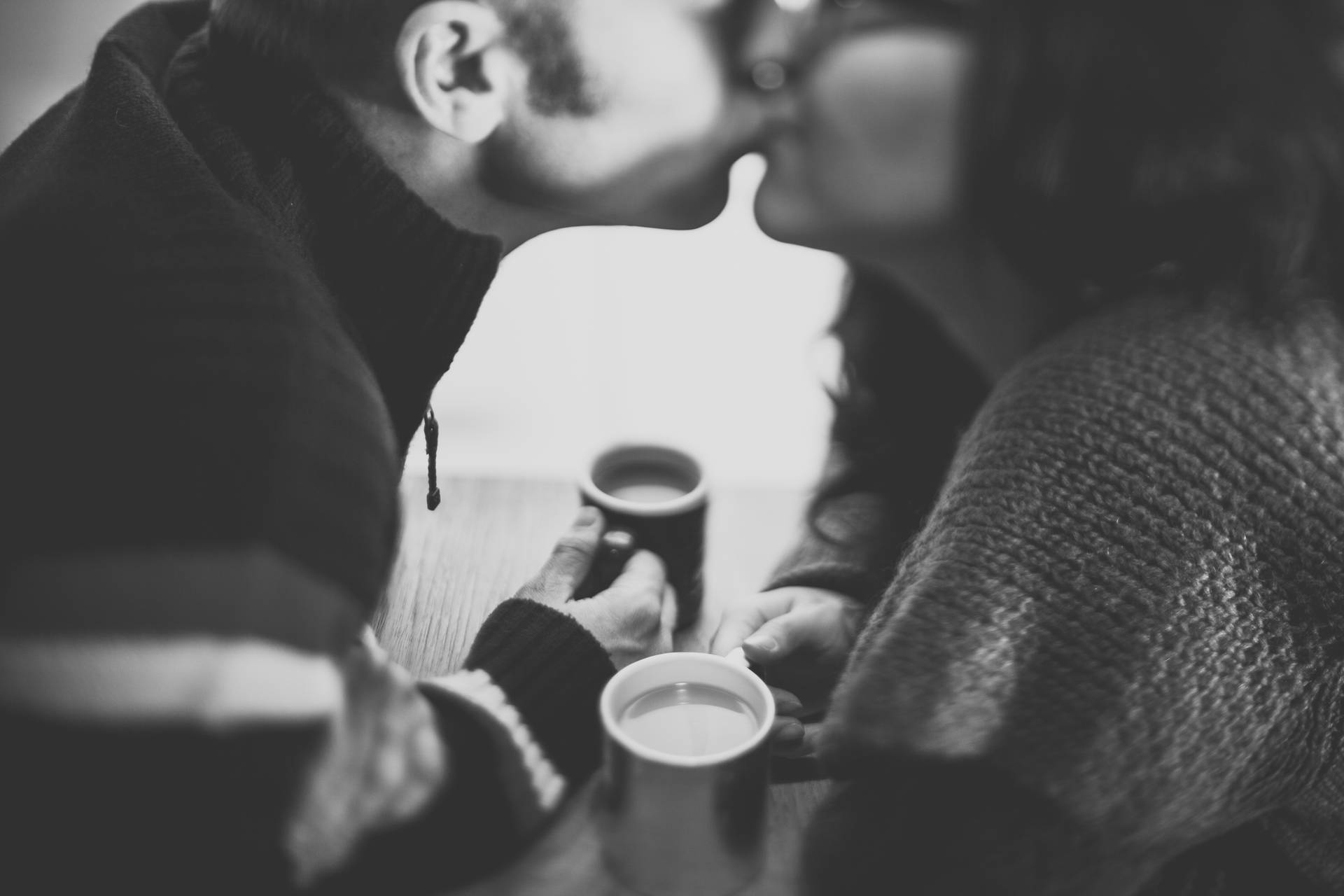 一對情侶在桌上拿著咖啡杯分享一個吻。