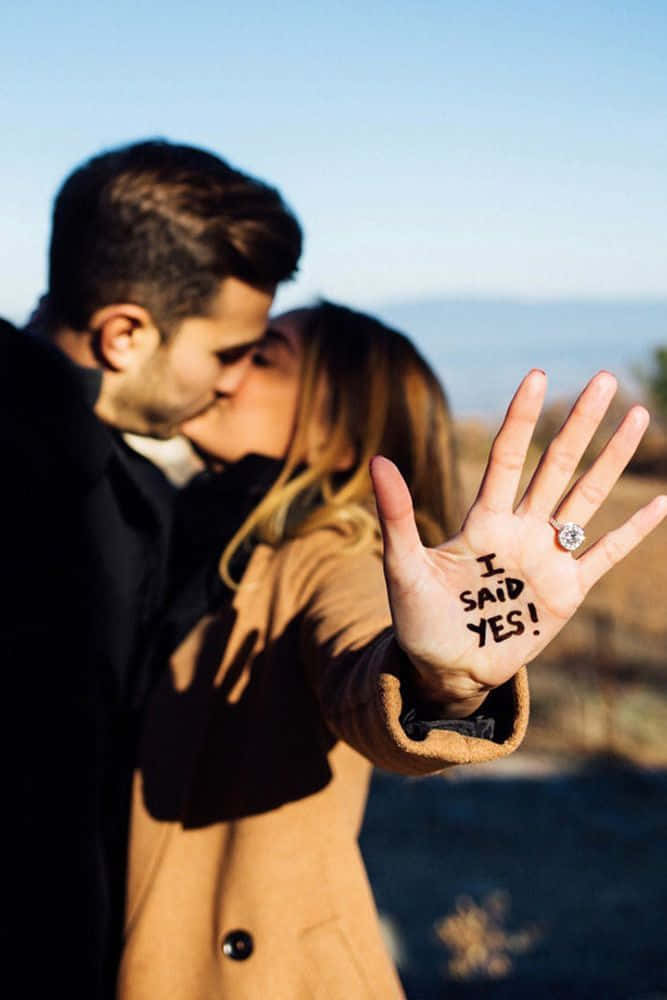 訂婚情侶接吻，她手上寫著「I SAID YES!」並展示戒指。