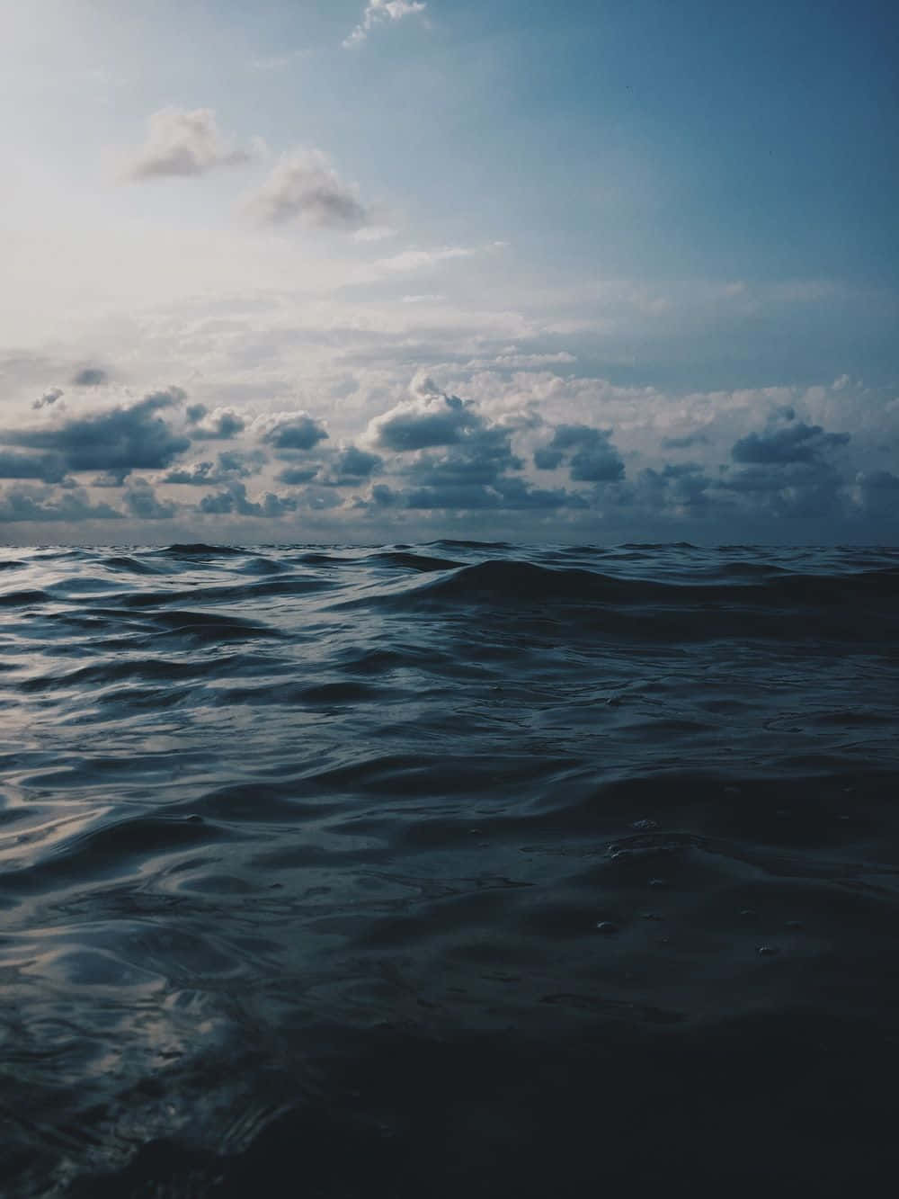 黃昏多雲的天空下深藍色的海洋波浪。