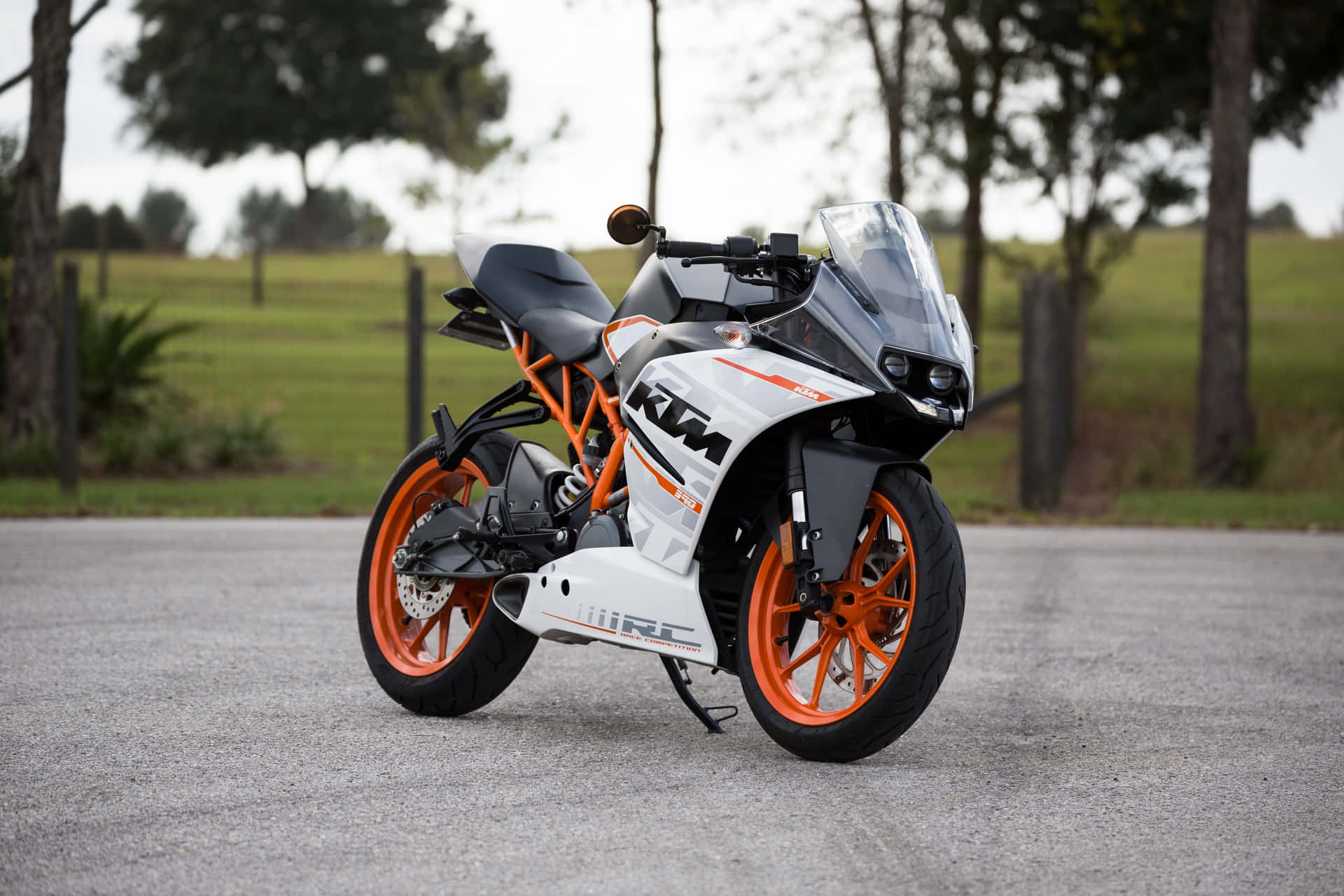 白色和橙色KTM RC電單車停泊在碎石路上，靠近樹木。