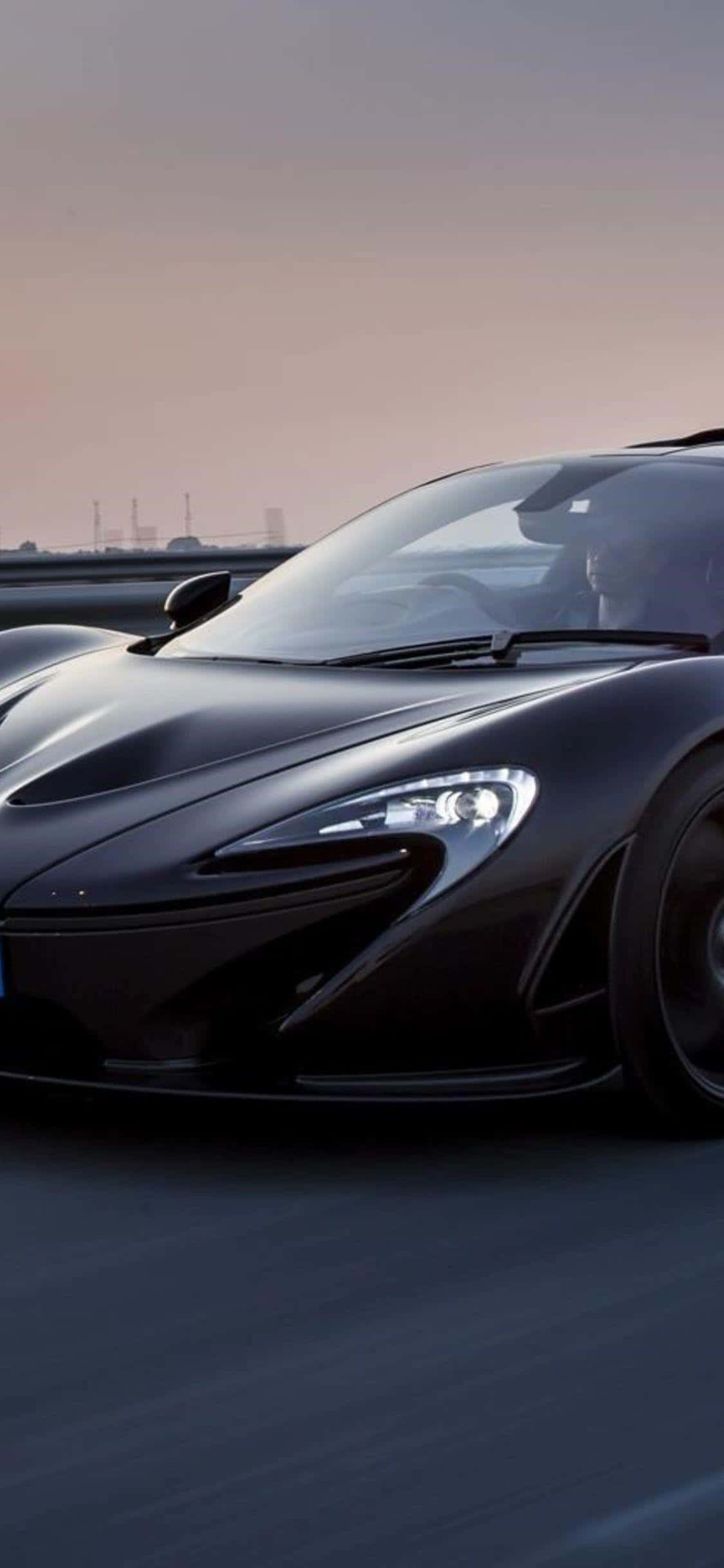 親身駕馭奢華 iPhone Xs McLaren 720S 壁紙 — 一輛時尚的黑色McLaren跑車在柔和暮色下的高速公路上高速行駛。