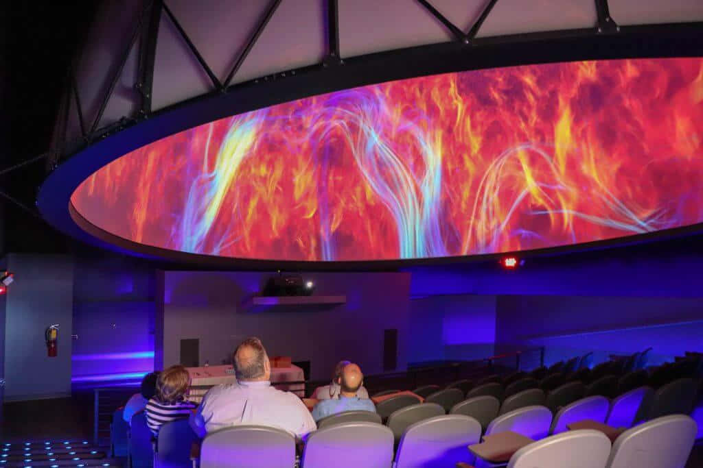Planetarium 桌布 壁紙 — 觀眾在漆黑的影院中觀看弧形穹頂屏幕上充滿活力的宇宙火焰表演。