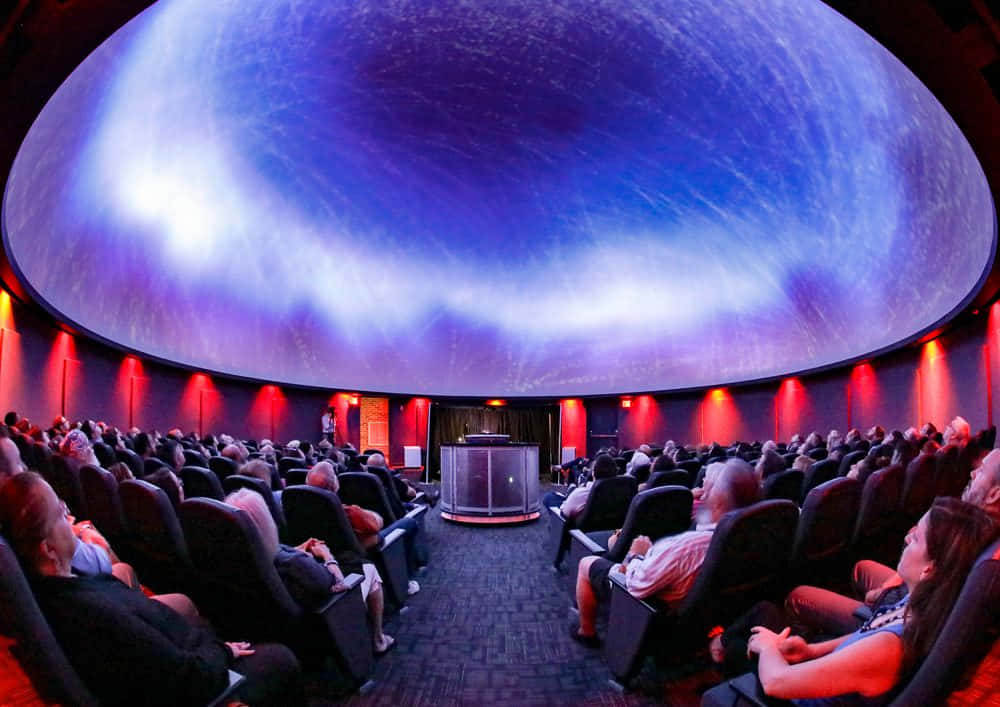Planetarium 桌布 壁紙 — 觀眾坐在天文館內，觀看弧形圓頂天花上的宇宙投影。