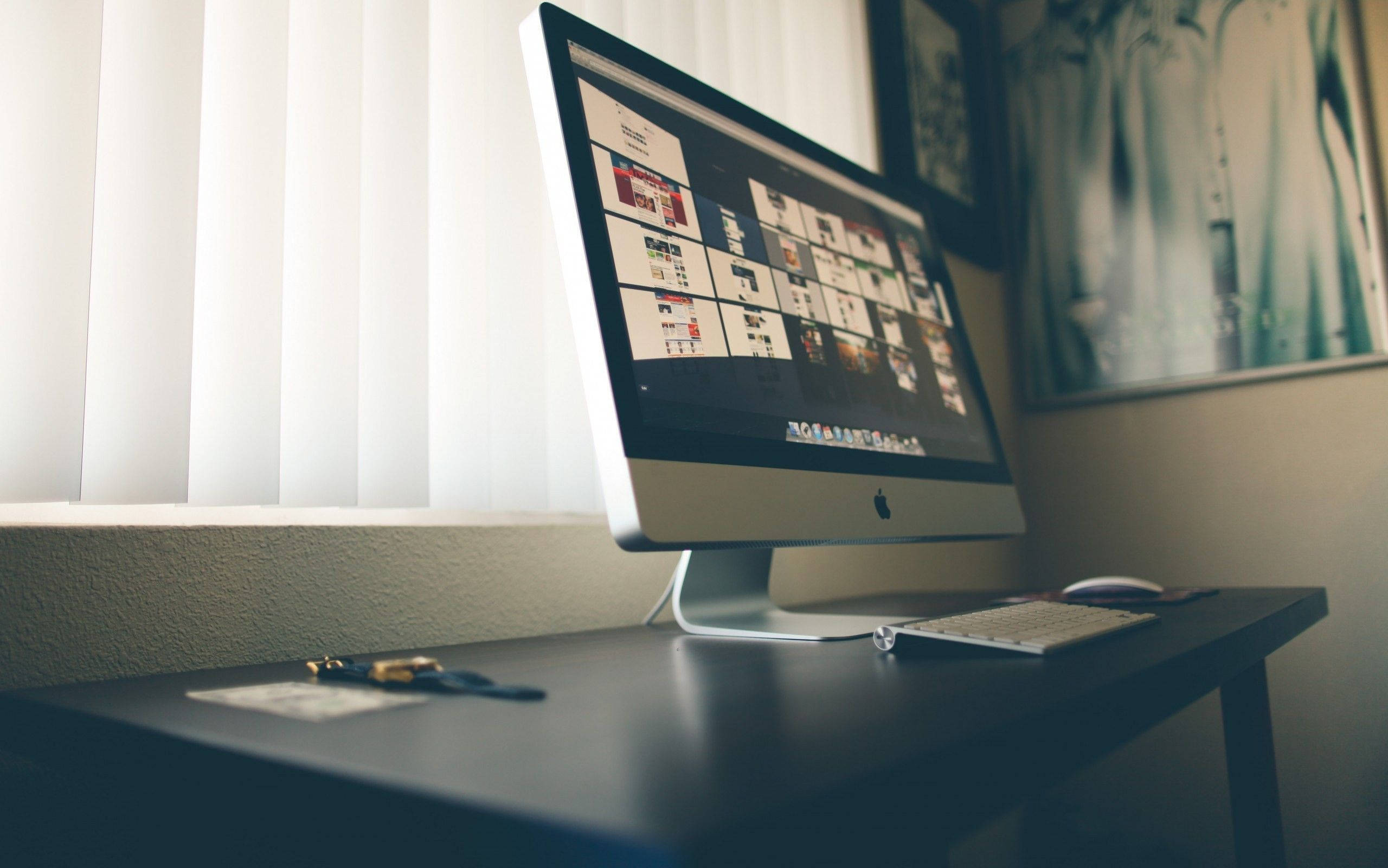 角落辦公桌配iMac 壁紙 — 一部時尚的iMac在深色桌子上顯示網站模擬圖的網格，旁邊有百葉窗和裱框藝術品。