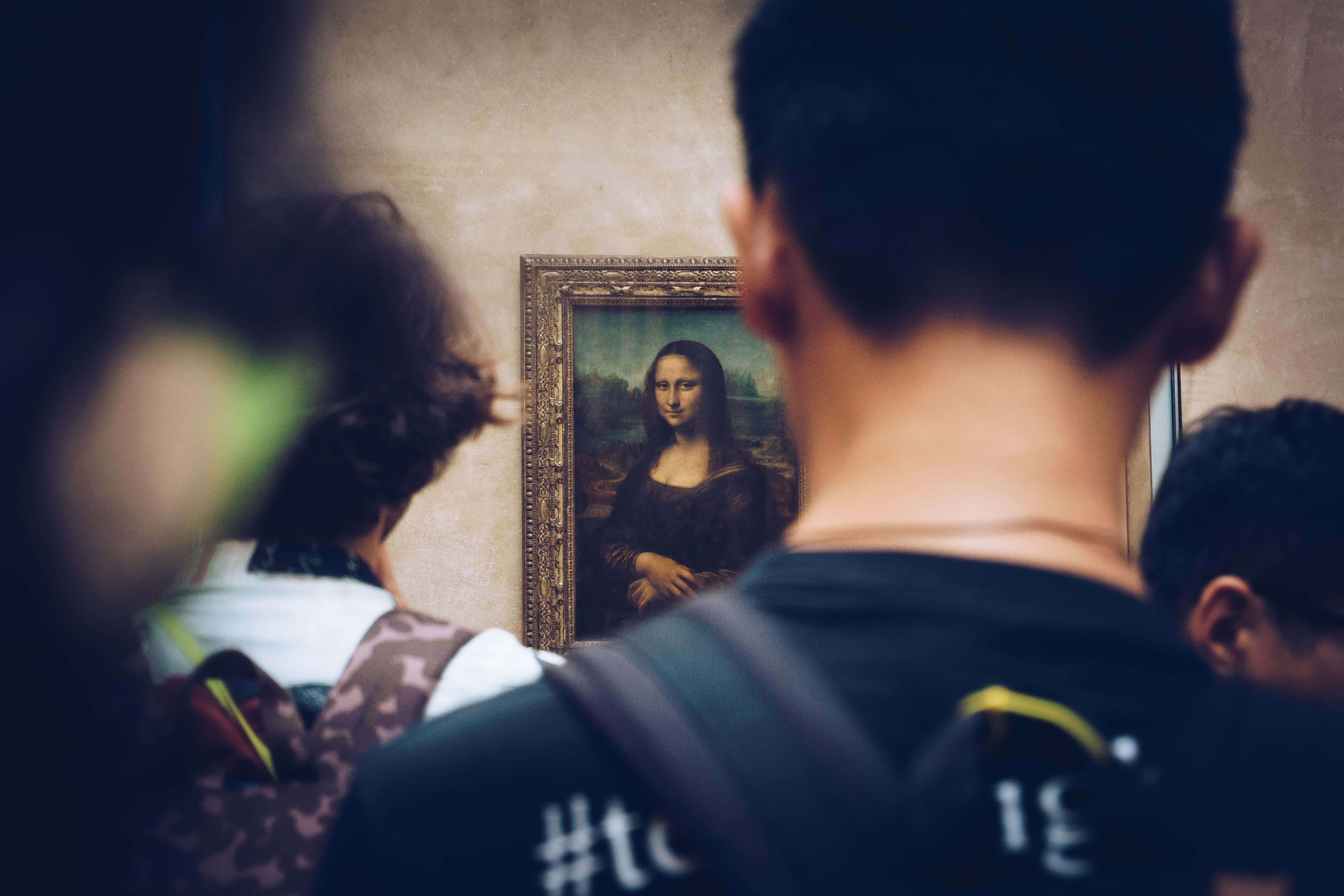 Mona Lisa 桌布 壁紙 — 訪客在博物館觀看帶有華麗畫框和模糊前景的蒙娜麗莎畫作。