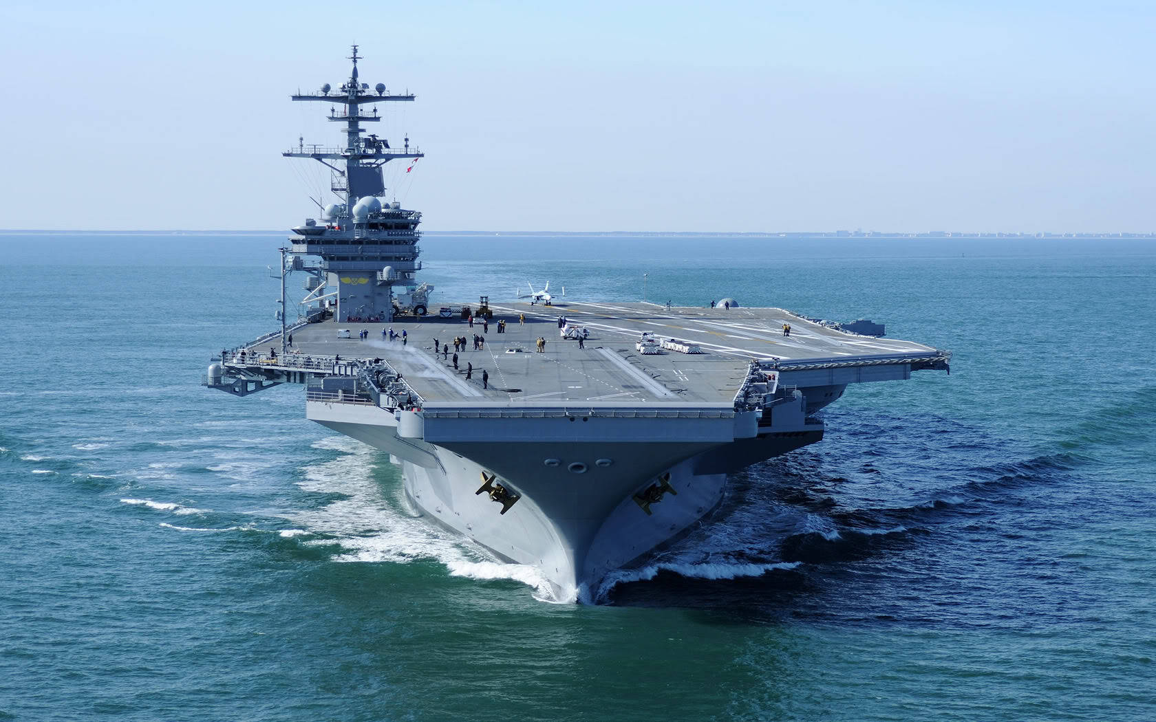 設有起降跑道的戰艦 壁紙 — 一艘巨大的灰色航空母艦在晴朗的天空下劃過深藍色的海水，留下白色的尾跡。