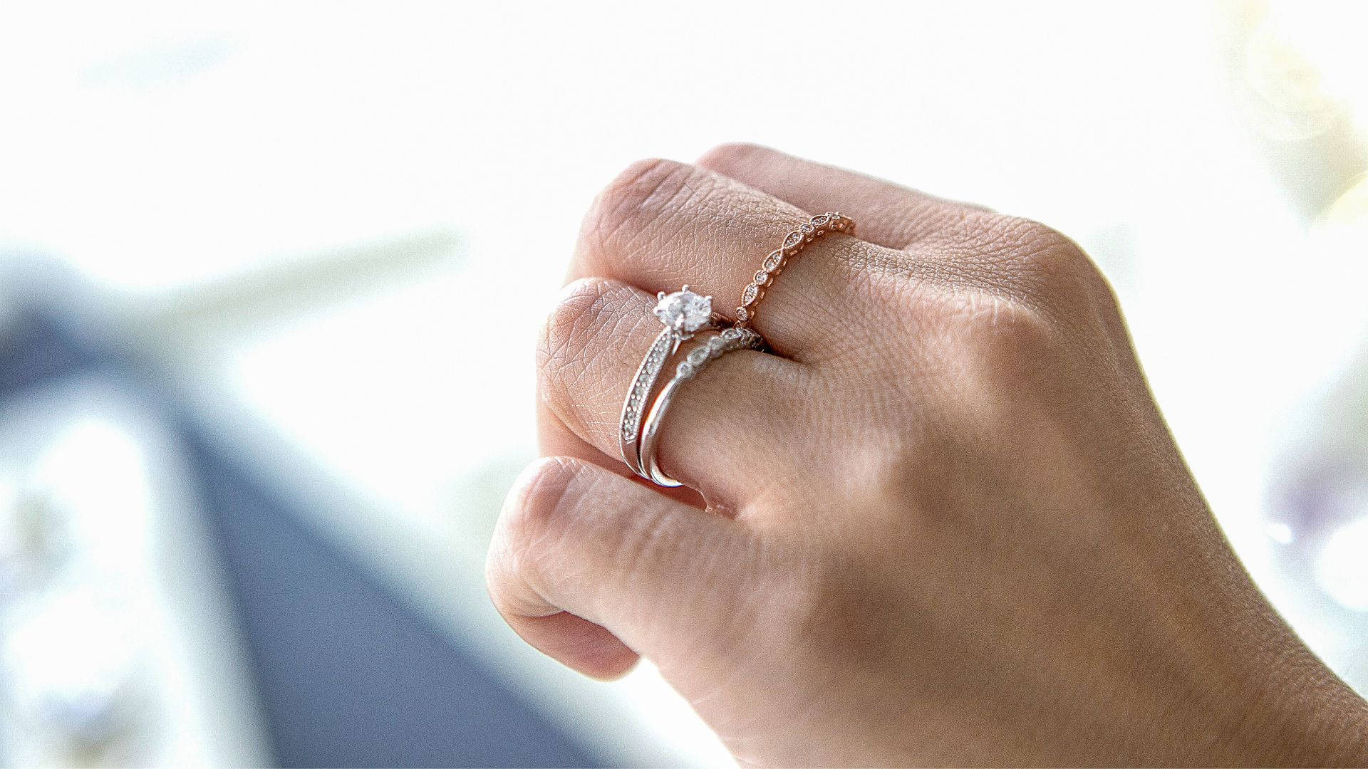 手展示兩枚結婚戒指，一枚單鑽戒指和一枚玫瑰金戒指。