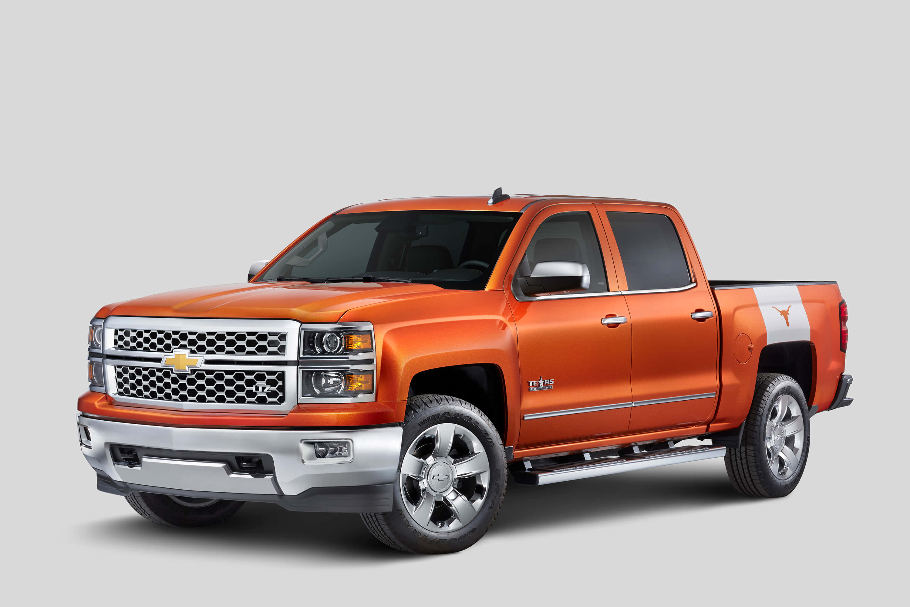 試駕您夢想中的雪佛蘭 壁紙 — 一輛充滿活力的橙色 Chevrolet Silverado 皮卡車，車斗側板上帶有 Texas Longhorns 標誌，在工作室燈光下展示。