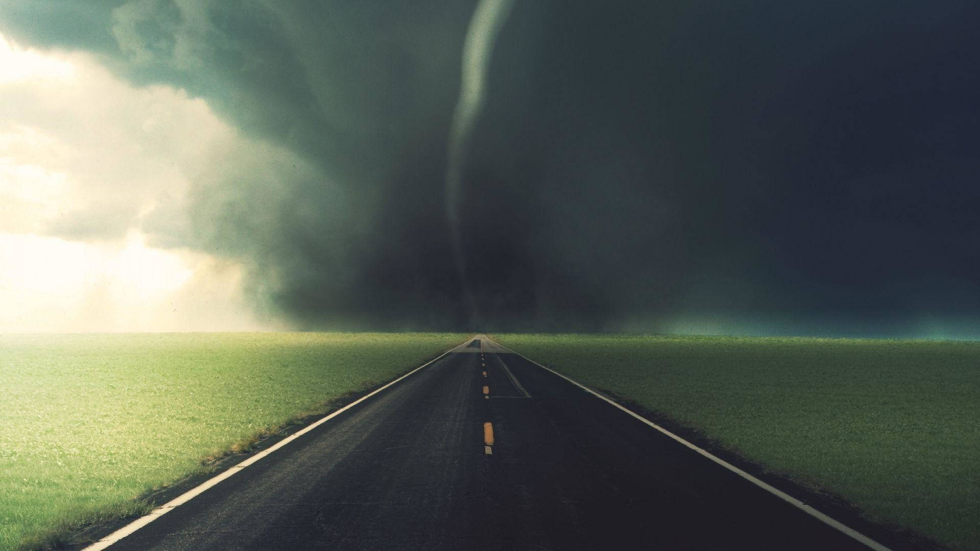 一條筆直的道路通向暴風雨天空下綠色田野中的一個巨大龍捲風。