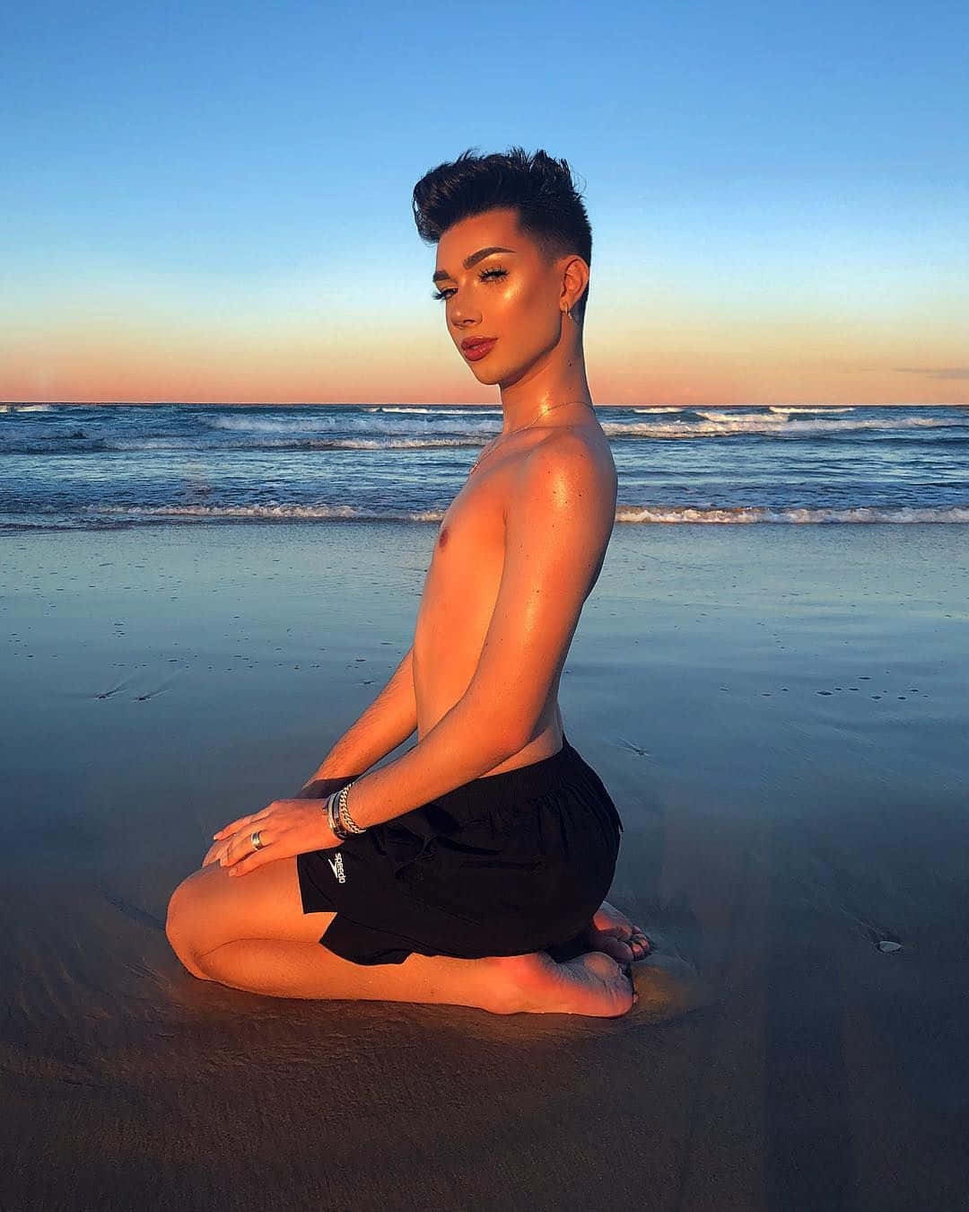 日落時分，一個人盤腿坐在沙灘上，身後有海浪。