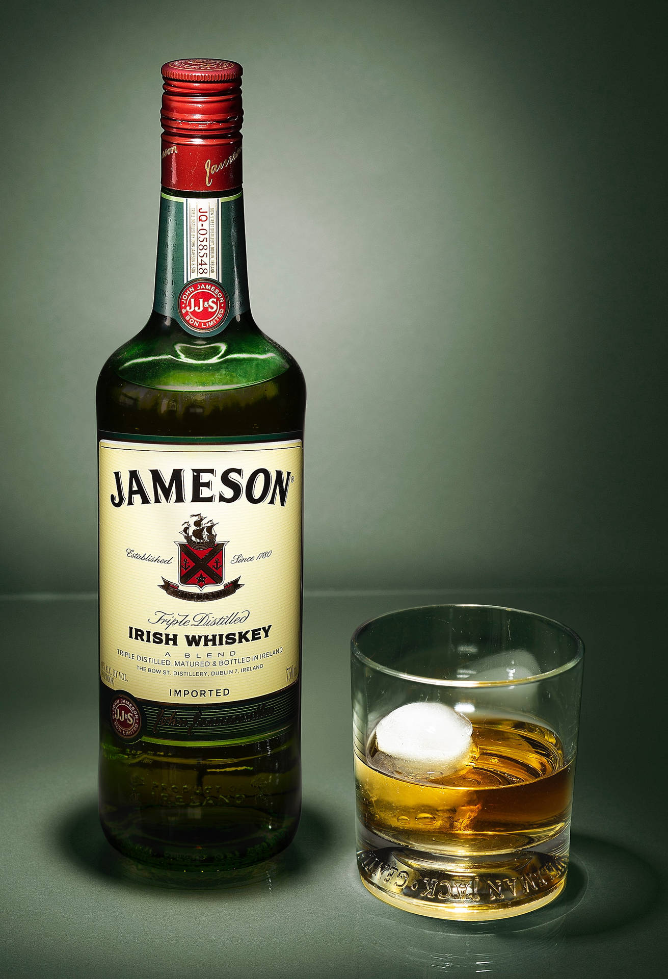 Jameson愛爾蘭威士忌酒瓶同杯，杯中有冰塊，放喺灰色表面上。