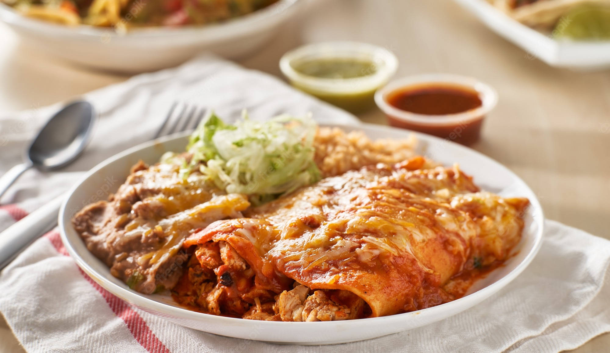 誘人奶油 enchiladas 美觀盛盤 壁紙 — 一盤芝士辣醬玉米餅，淋上紅醬，撒上生菜絲，放在條紋餐巾上，旁邊有蘸醬。