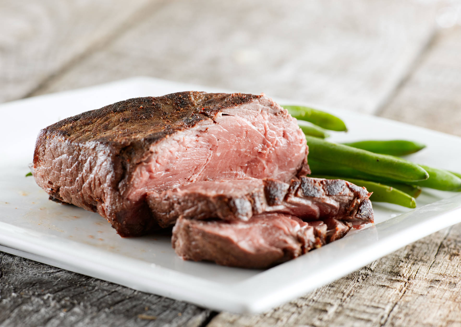切片嘅 medium-rare 牛扒配青豆，放喺白色碟上，擺喺木質表面。