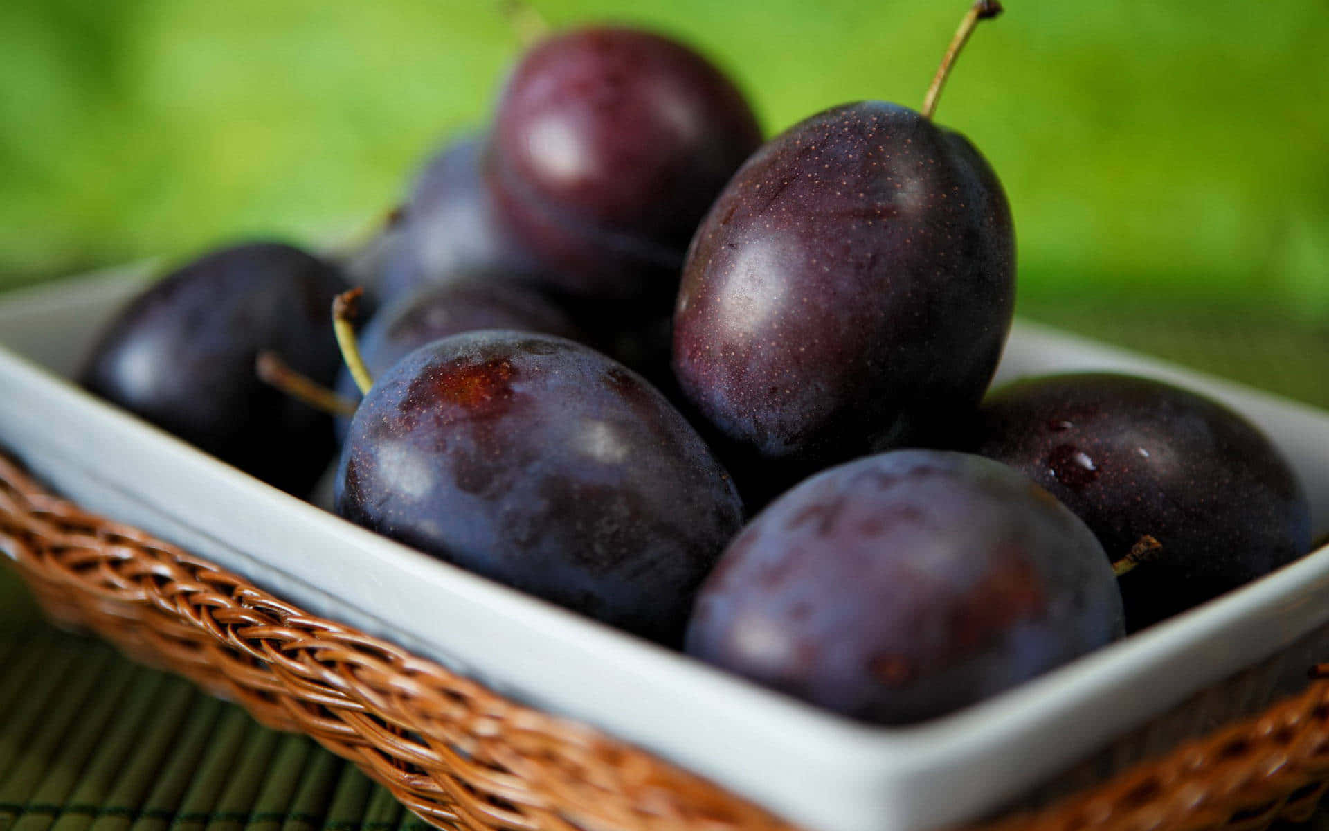 一碗新鮮的深紫色李子放在編織墊上。