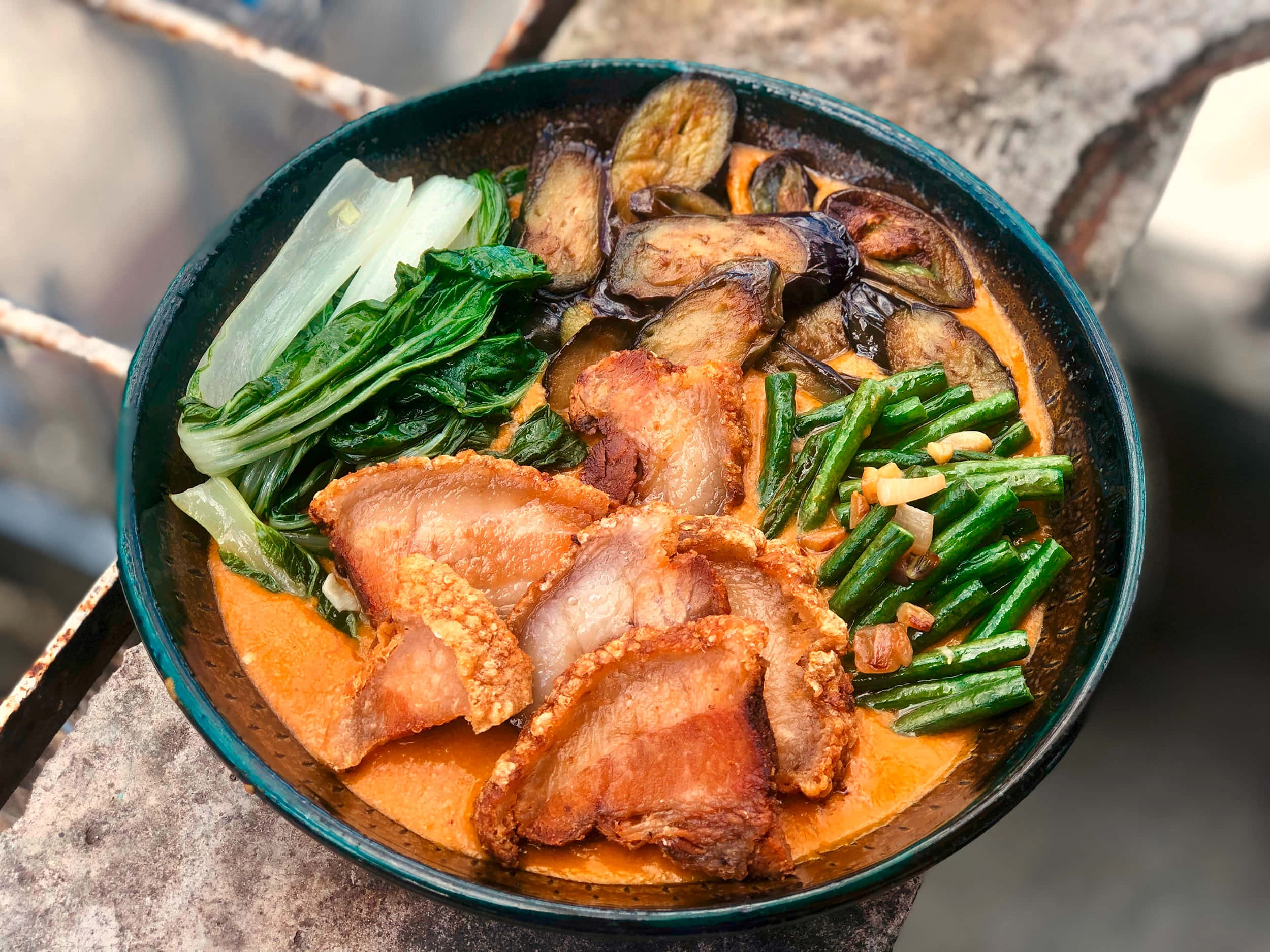 誘人的菲律賓菜式 Kare-Kare 壁紙 — 一碗熱騰騰的濃郁橙色咖喱，配上香脆豬腩肉、烤茄子及鮮綠色蔬菜。