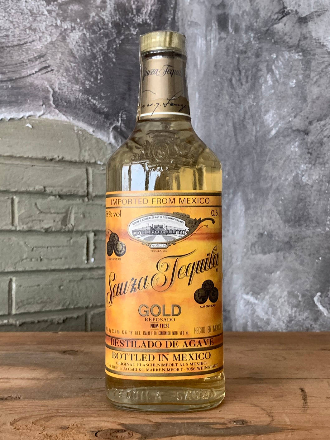 Sauza Gold Tequila 酒瓶放在木桌上，背景是磚牆。
