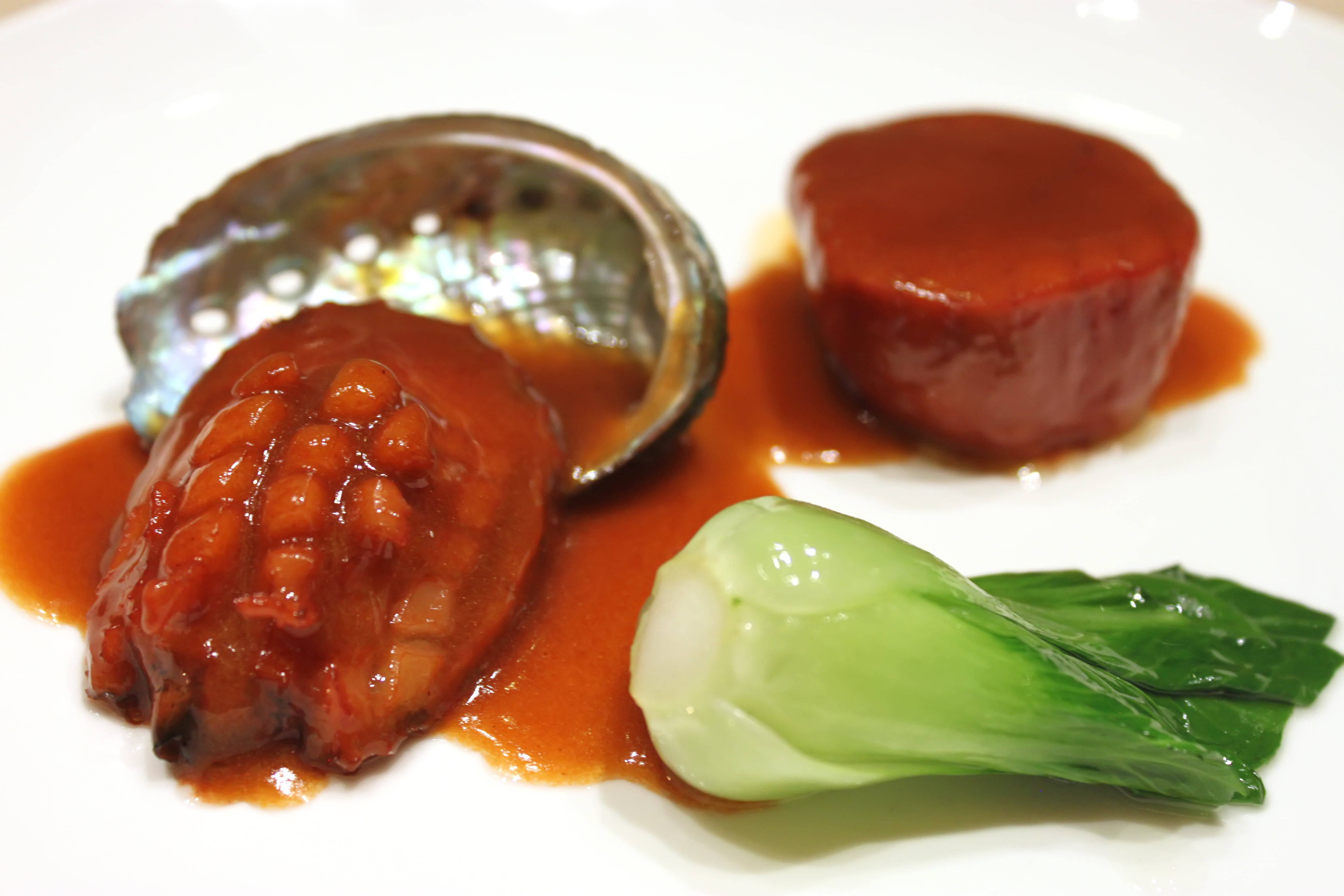 誘人鮑魚高級料理 壁紙 — 光澤鮑魚配上濃郁醬汁，旁邊有白菜和圓形陶罐，盛載在潔白無瑕的碟子上。