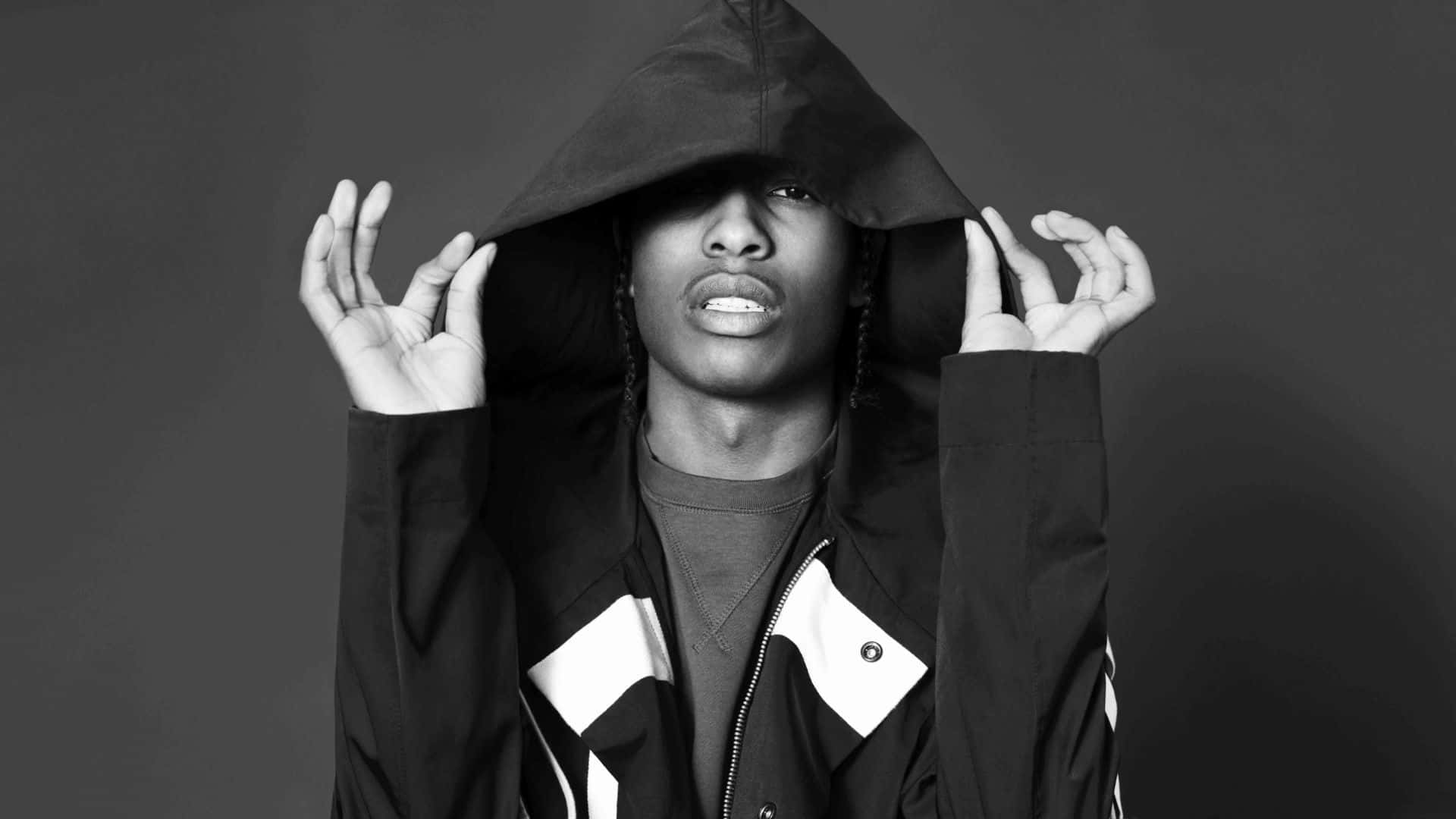 說唱歌手 Asap Rocky 對鏡擺拍 壁紙 — 一個穿著連帽外套的人掀起帽子，在深灰色背景上露出銳利的眼睛和張開的嘴巴。