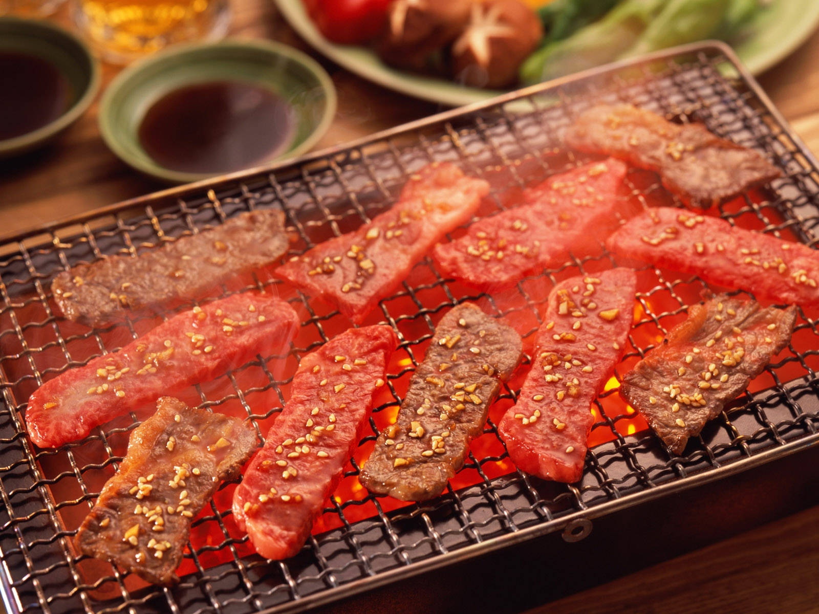 滋滋作響嘅牛肉同生肉喺烤架上，配上芝麻同配菜。