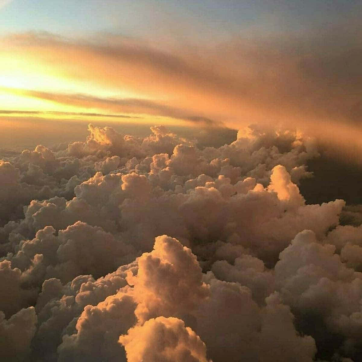 請花點時間欣賞大自然的壯麗 壁紙 — 從高空俯瞰蓬鬆的雲朵沐浴在金色日落光芒中，上方是柔和的橙色和藍色天空。