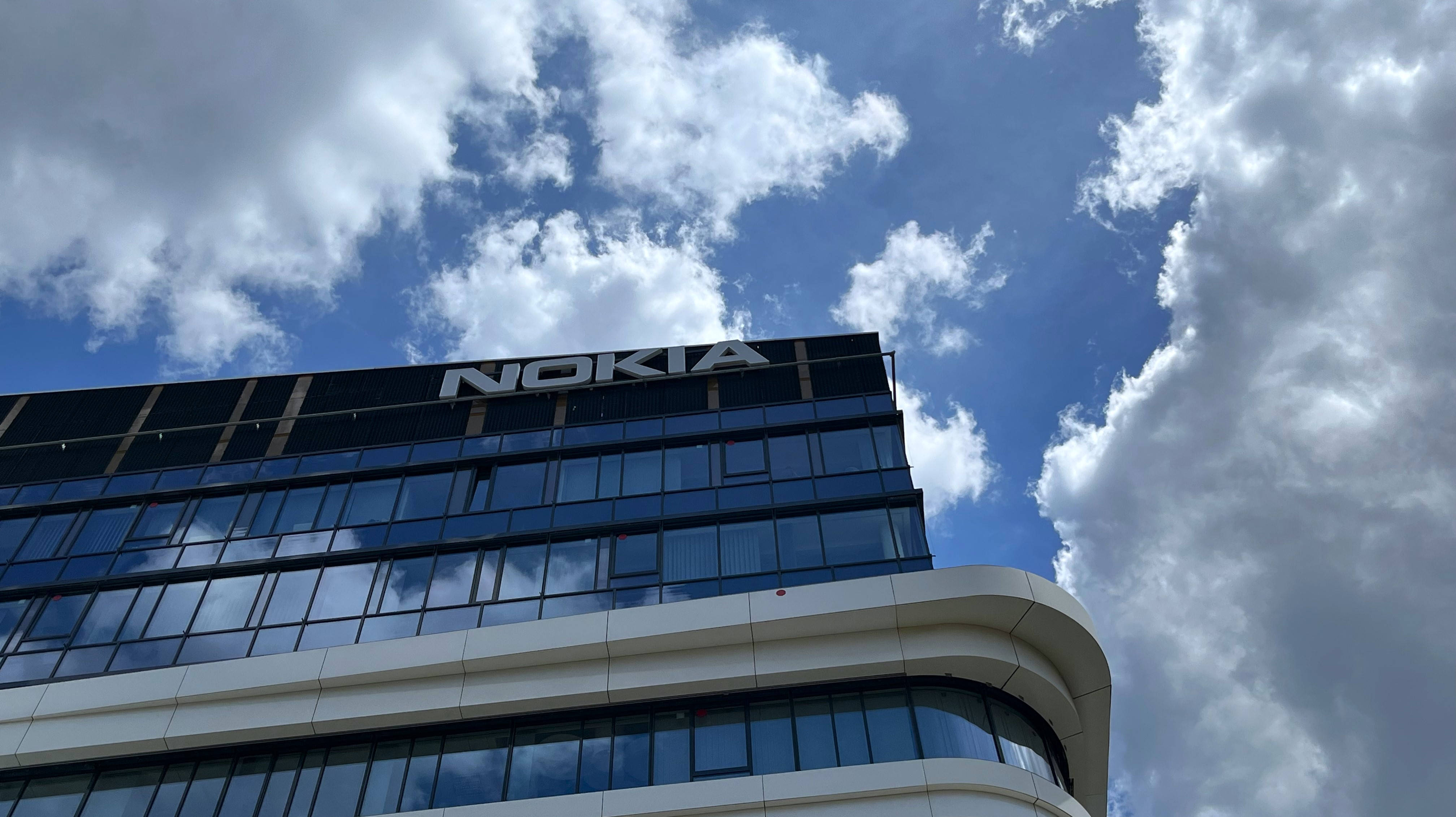 諾基亞網路 Skypark 大樓 壁紙 — 一座現代玻璃摩天大樓，帶有顯眼的Nokia標誌，聳立在充滿蓬鬆白雲的鮮豔藍天下。