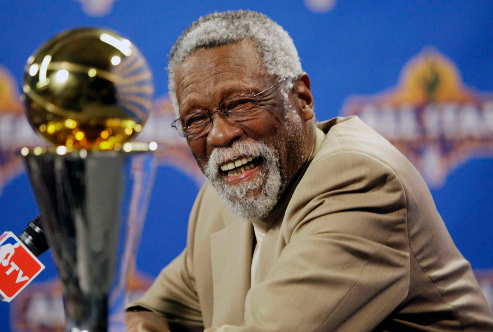戴眼鏡的長者在NBA冠軍獎盃旁大笑。