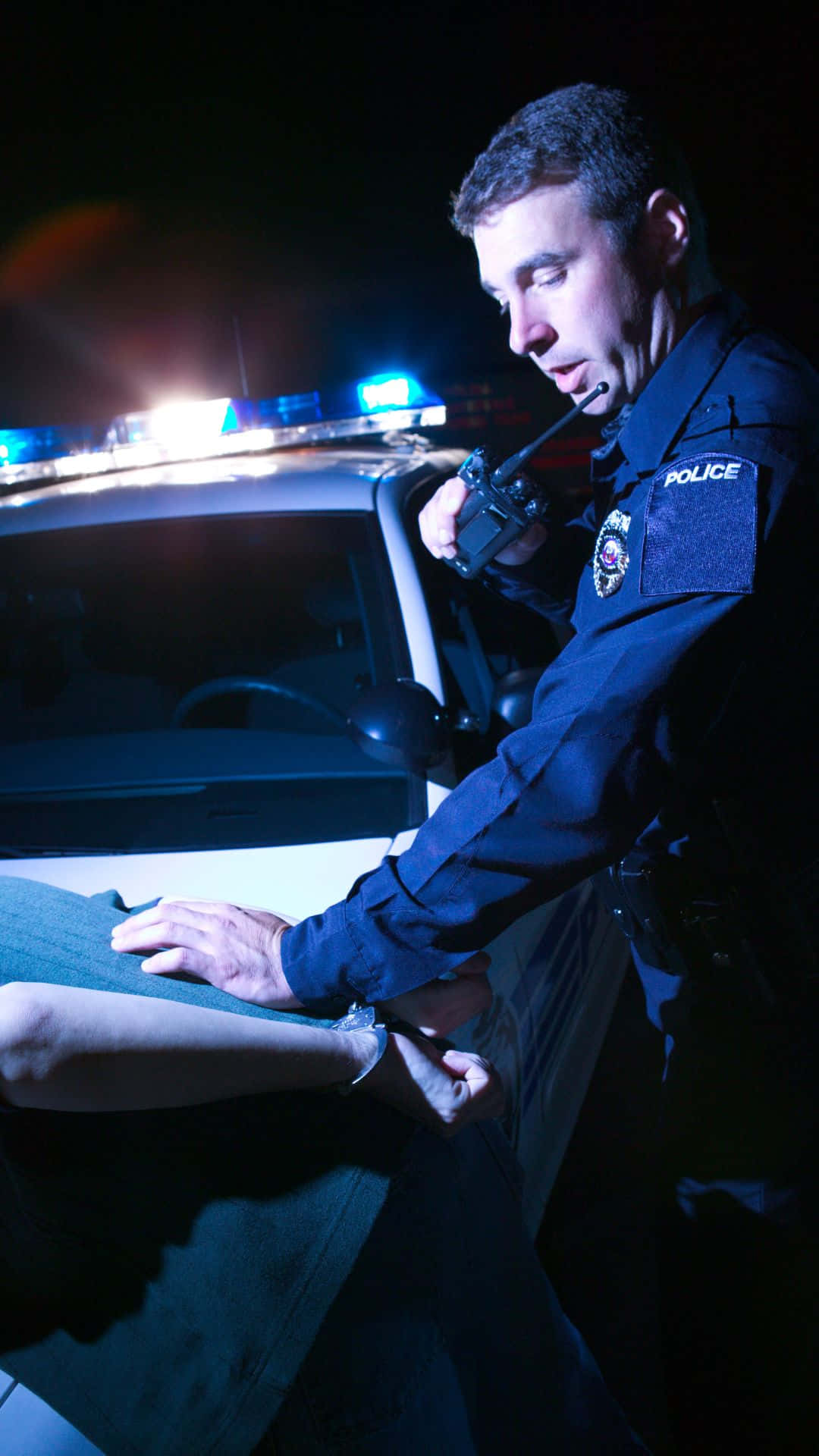 警察在夜間於巡邏車旁給一個人上手銬。