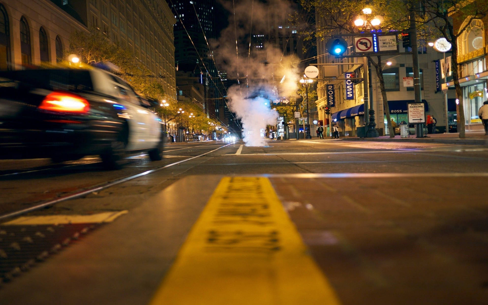 警車在夜間駛過城市街道，蒸汽上升，黃色警示帶可見。