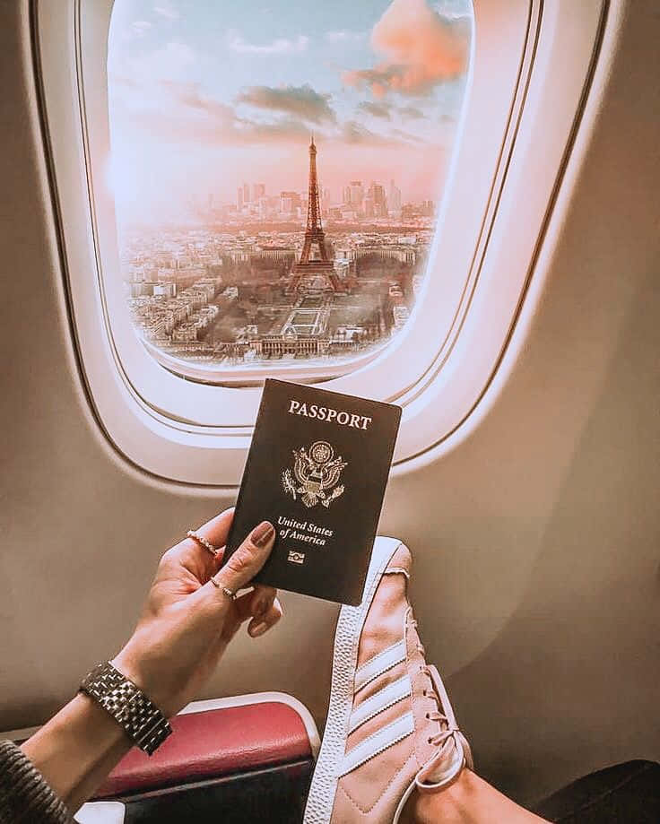 護照功能全覽 壁紙 — 一名旅客在飛機窗前手持美國護照，俯瞰巴黎，背景是日落時分的艾菲爾鐵塔。