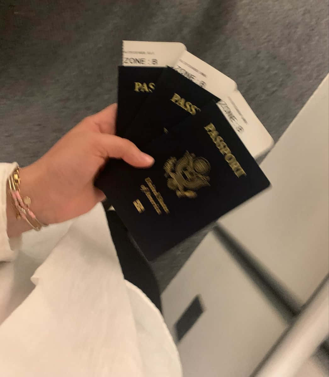護照對抗木質背景，揭開新旅程 壁紙 — 一隻手拿著多本美國護照和登機證，背景是模糊的機場閘口。