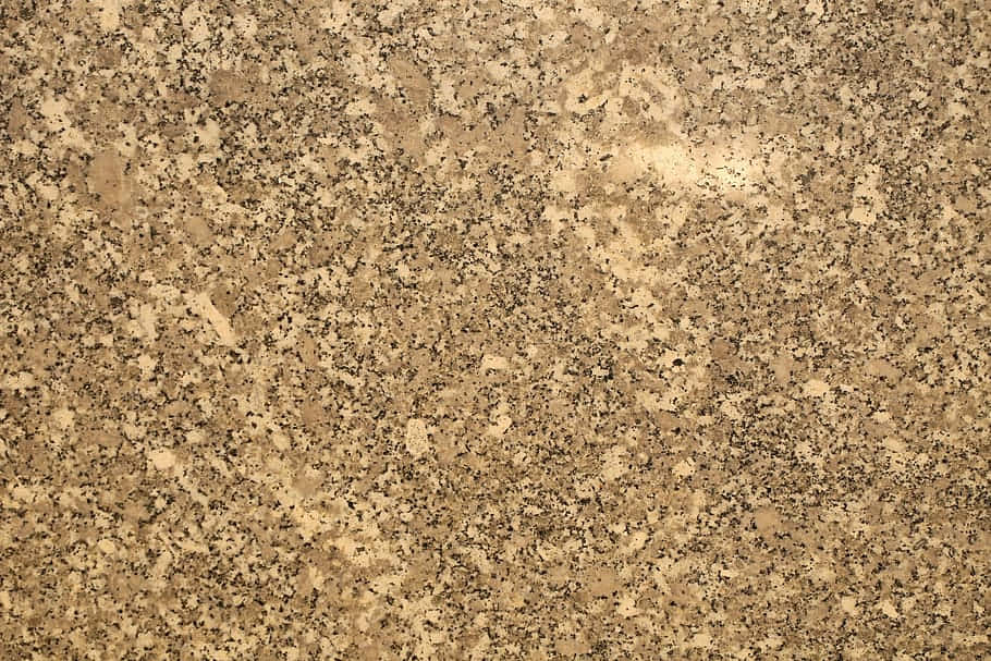 變質岩花崗岩的紋理 壁紙 — 金色棕色花崗岩嘅特寫，喺均勻光線下有黑色同米色斑點礦物顆粒。