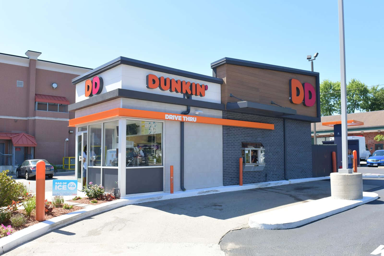 讓 Dunkin' Donuts 的美味驚艷您的味蕾 壁紙 — 一個晴朗的日子，在現代化的Dunkin'得來速，帶有橙色點綴和清澈的藍天。