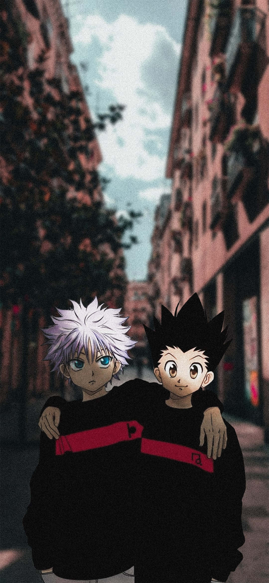 讓 Gon 與 Killua 的動人組合為你的手機增添刺激與樂趣！ 壁紙 — 兩個穿著帶有紅色條紋的黑色連帽衫的動漫男孩，在多雲的天空下，手臂挽著手臂站在狹窄的城市小巷裡。