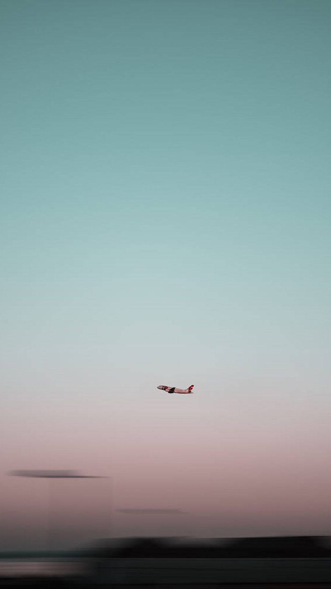 一架飛機在柔和的日落天空背景下飛行，下方是模糊的地面。
