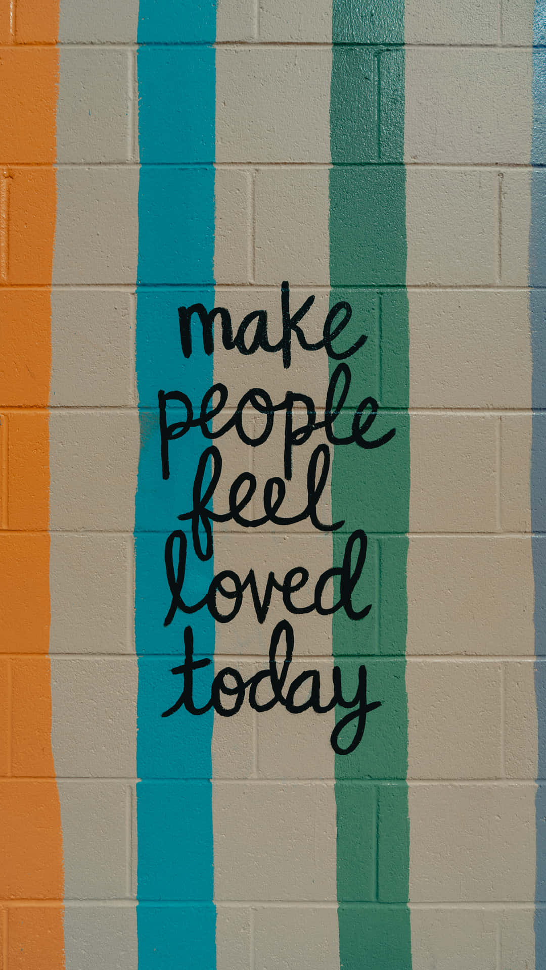 一面彩色條紋牆，上面用黑色草書寫著 make people feel loved today 的訊息。