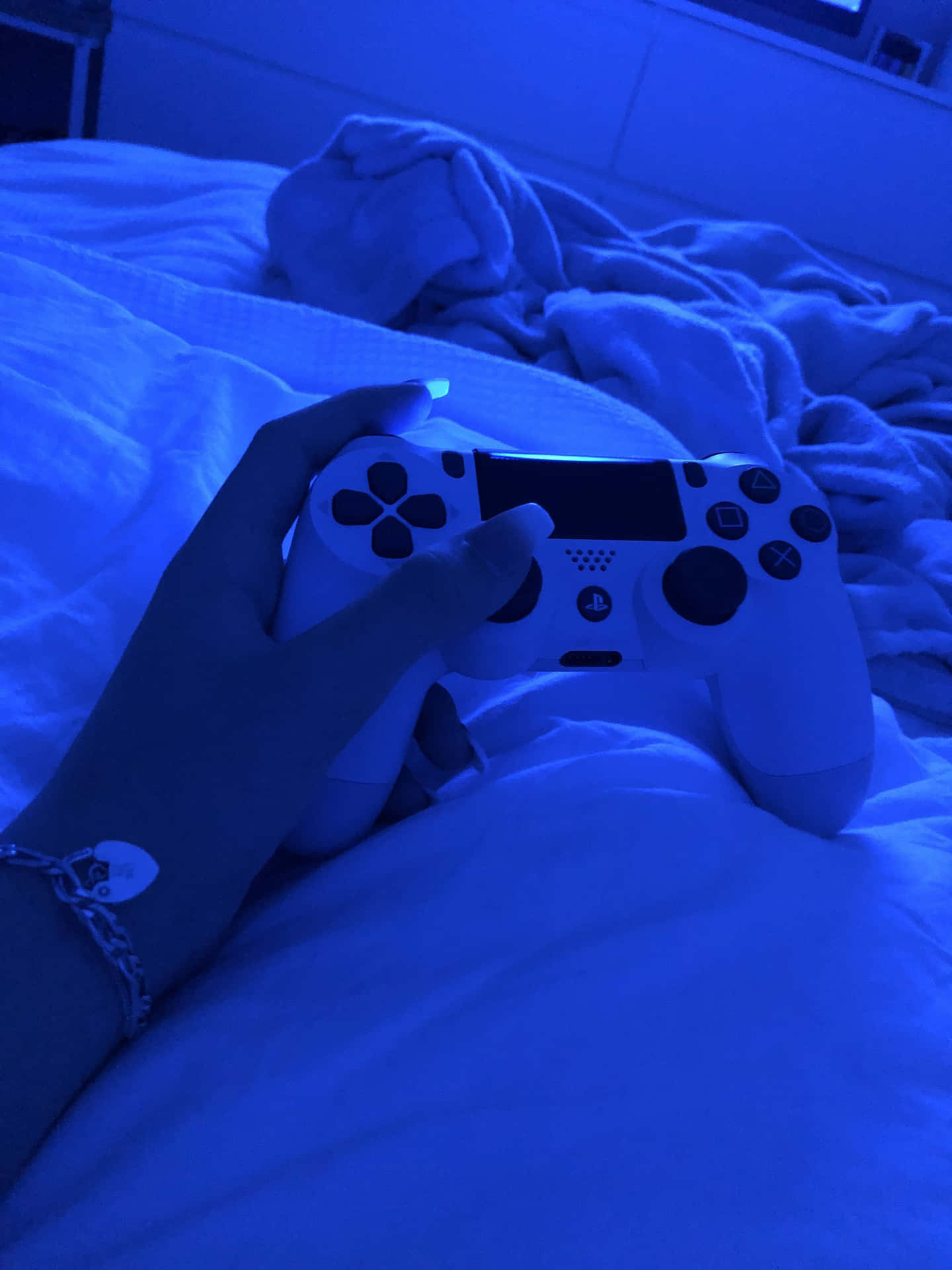 手在藍光下在床上握著白色遊戲控制器