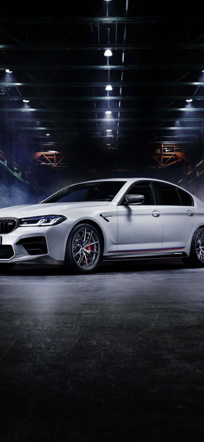 白色BMW M5跑車在光線昏暗的工業車庫中，配有聚光燈和煙霧。